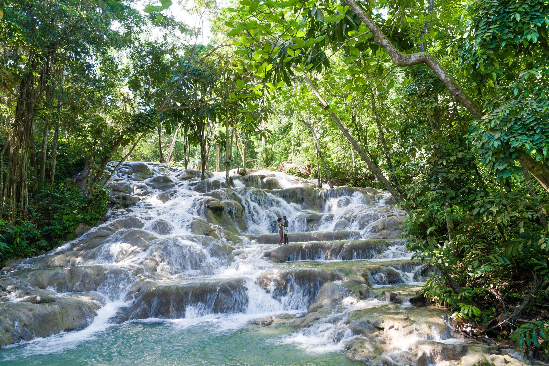 Guests standing on tiered waterfall rocks in the forest near Sandals Dunns River.