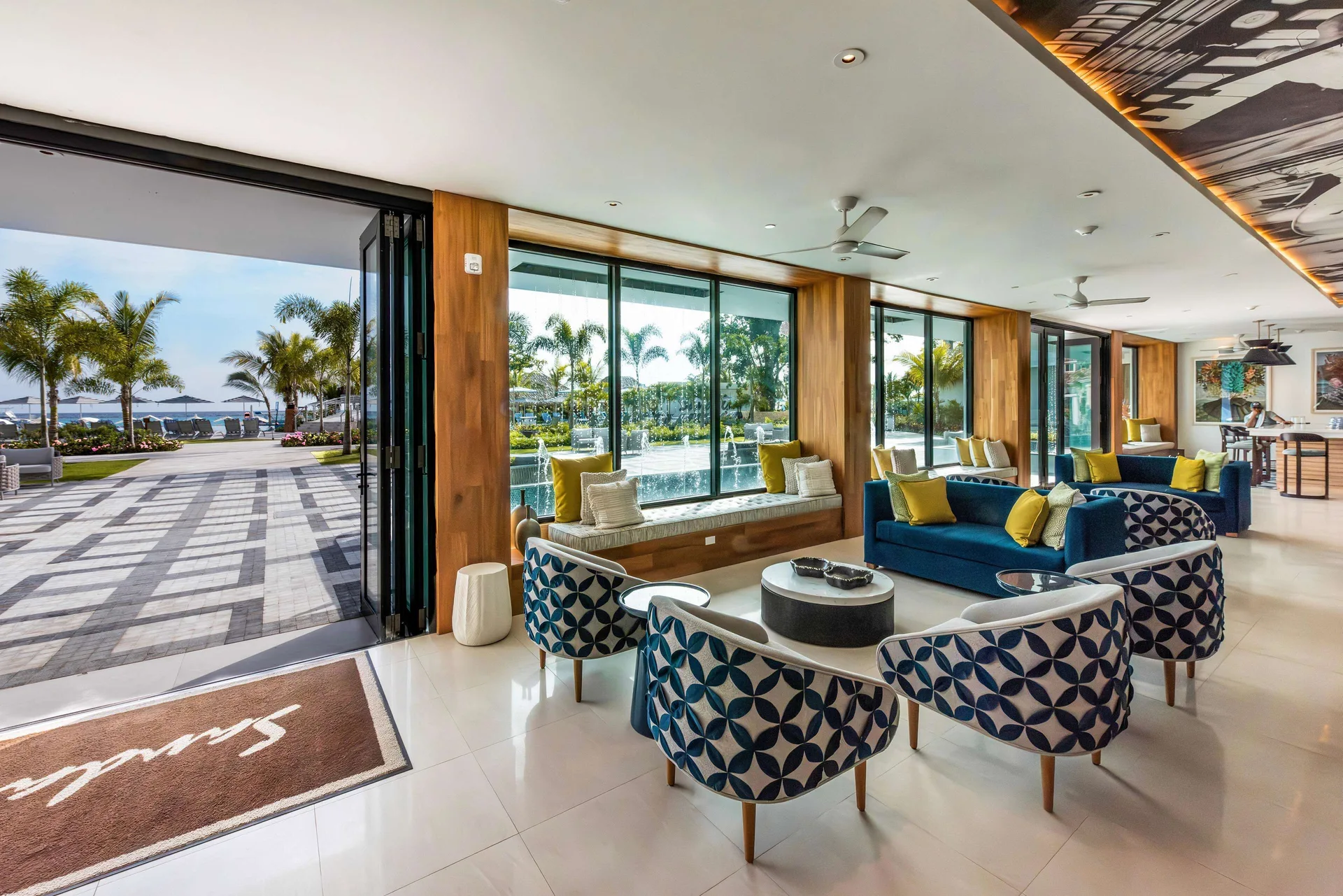 Indoor lounge with blue sofas, patterned chairs, glass walls, and ocean-facing doors at Sandals Dunns River.