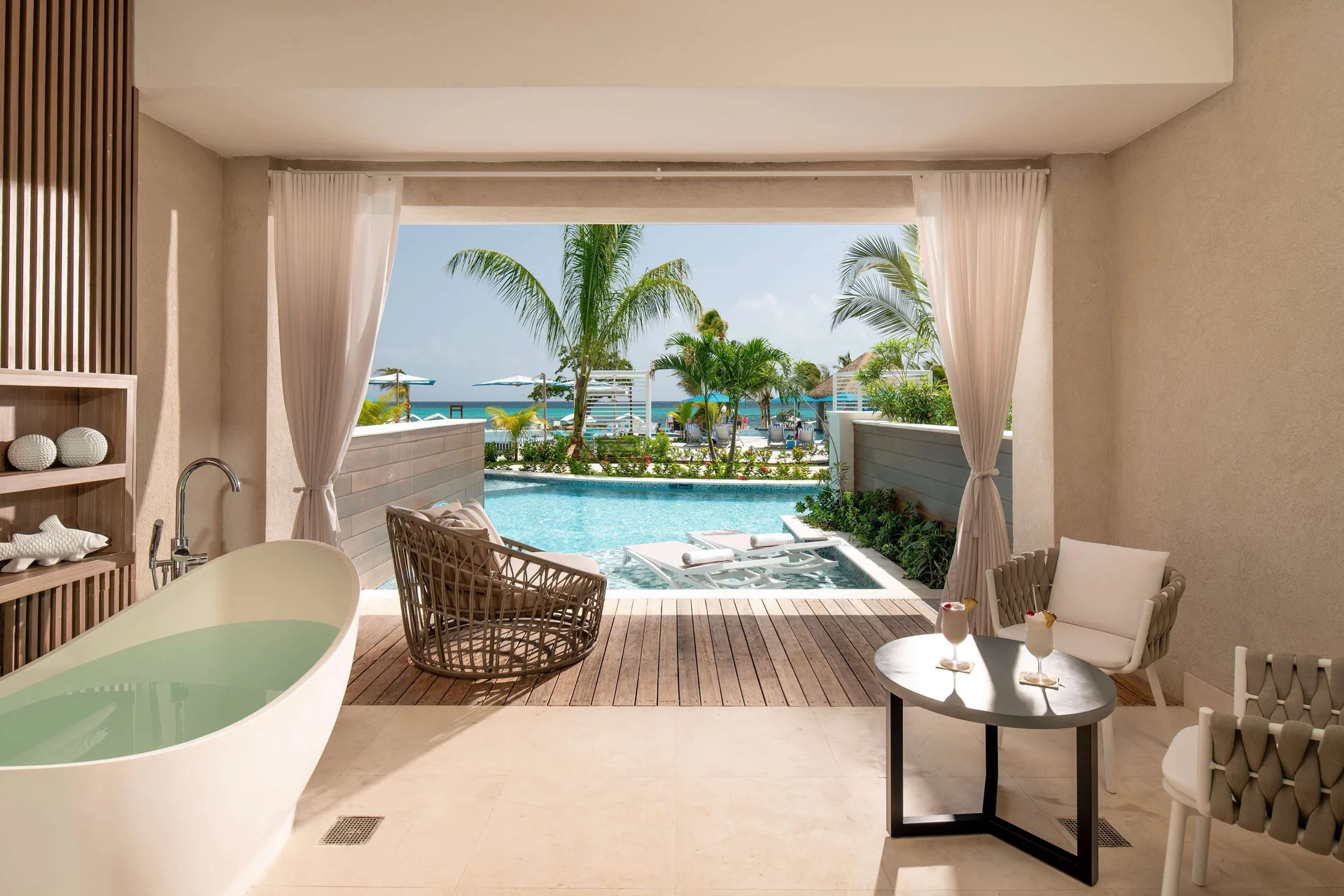 Covered patio at Sandals Dunns River with soaking tub, chairs, swim-up pool, and ocean beyond.