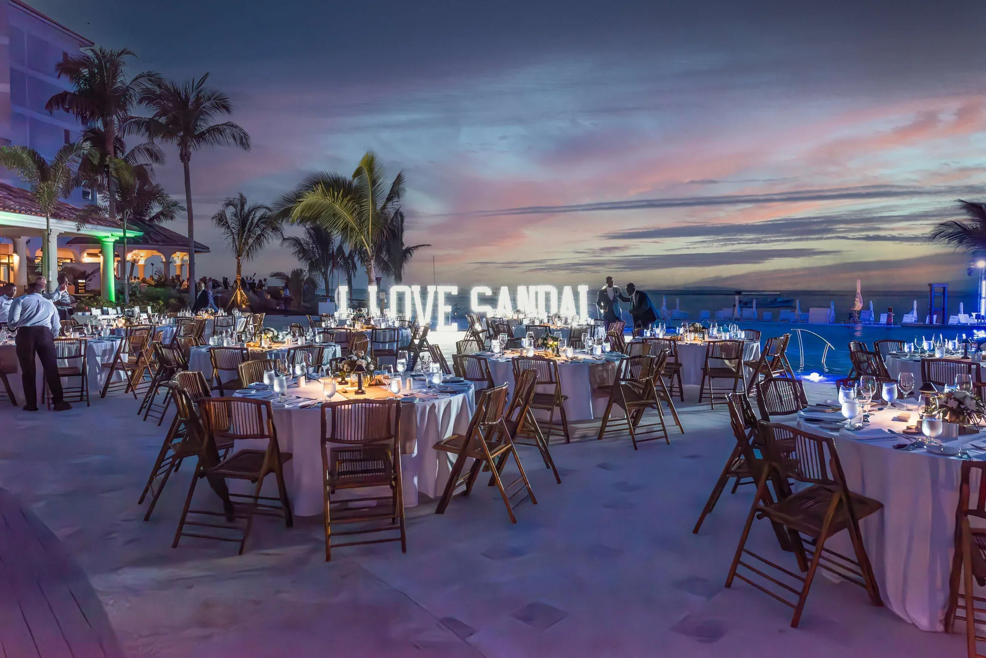 Outdoor evening event with round tables by the pool and ocean at Sandals Dunns River.