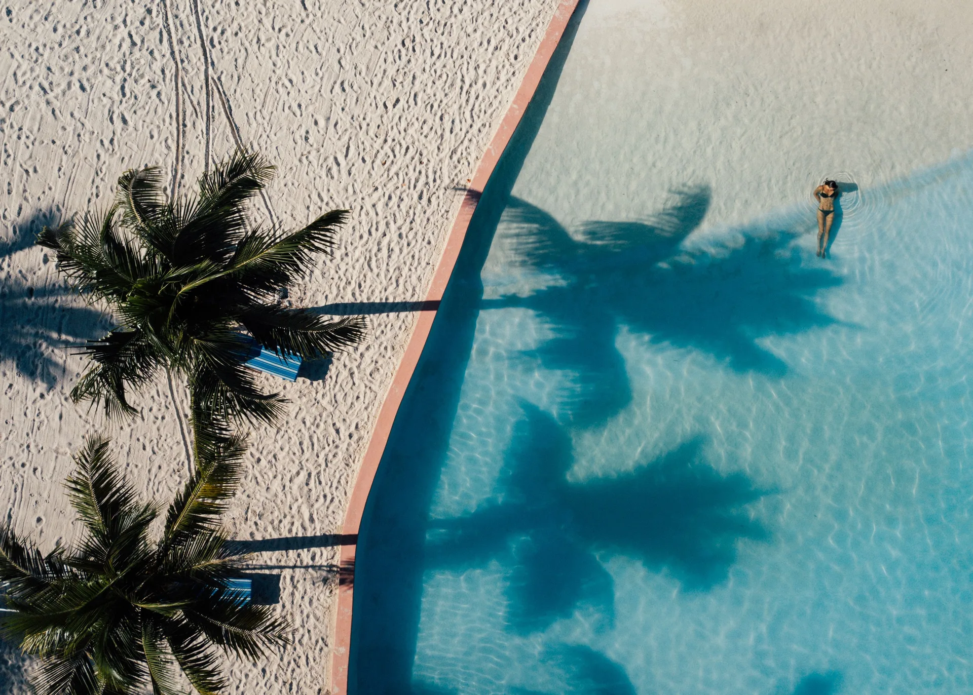 An aerial view shows palms, sand, pool water, and a swimmer at Sandyport Beach Resort.