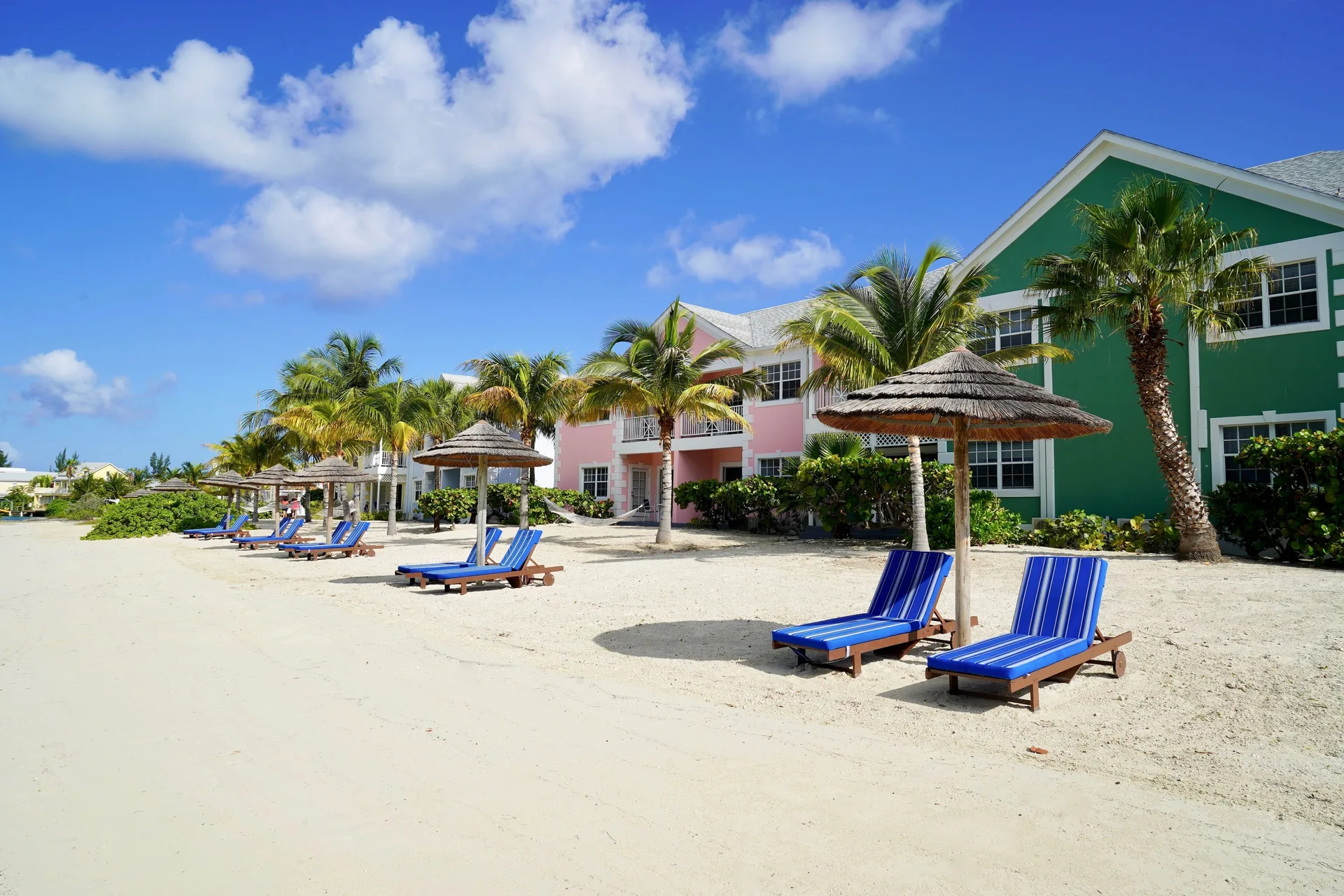 Beach loungers and thatched shades outside colorful buildings at Sandyport Beach Resort.