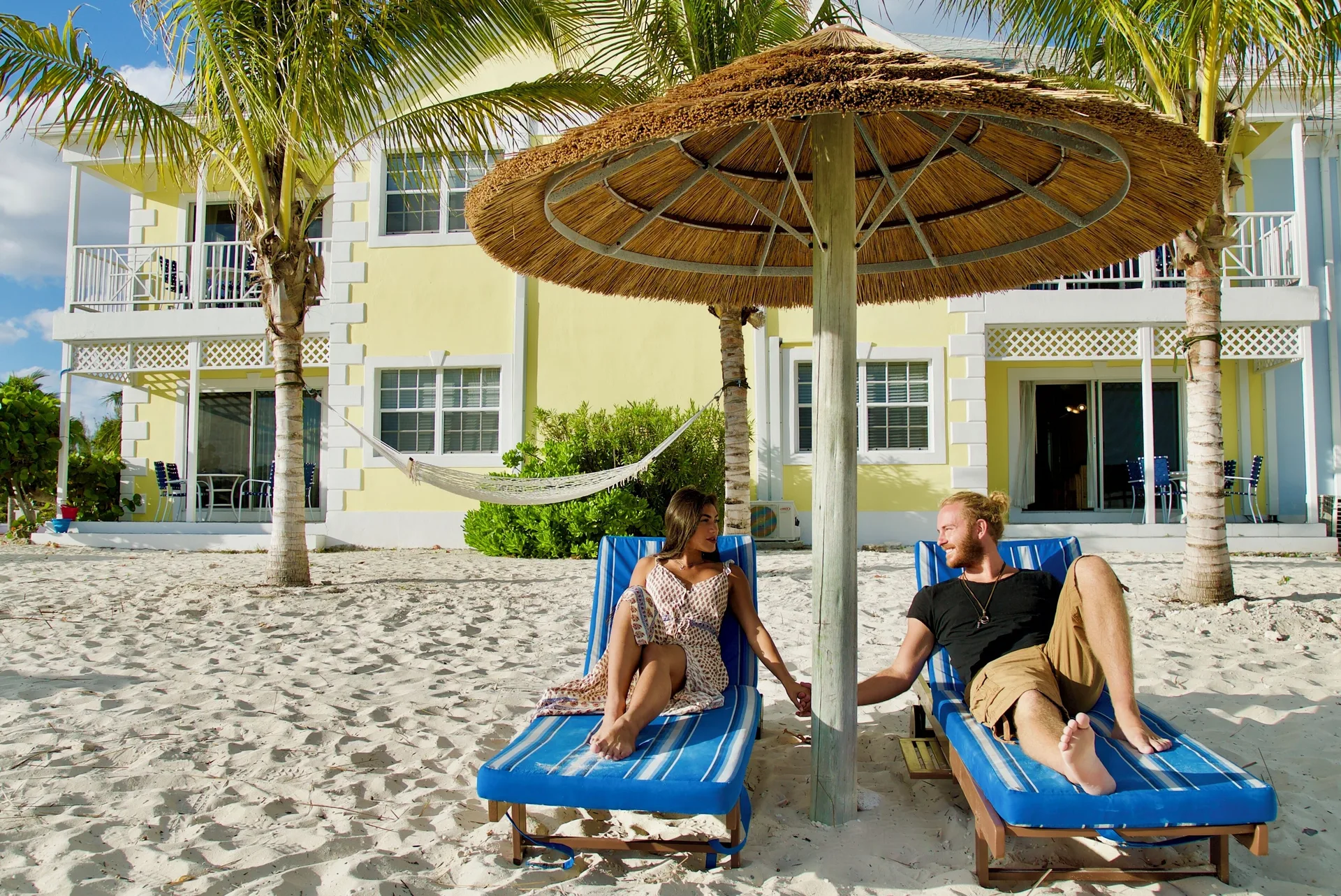 Couple relaxing on blue beach loungers outside rooms at Sandyport Beach Resort.