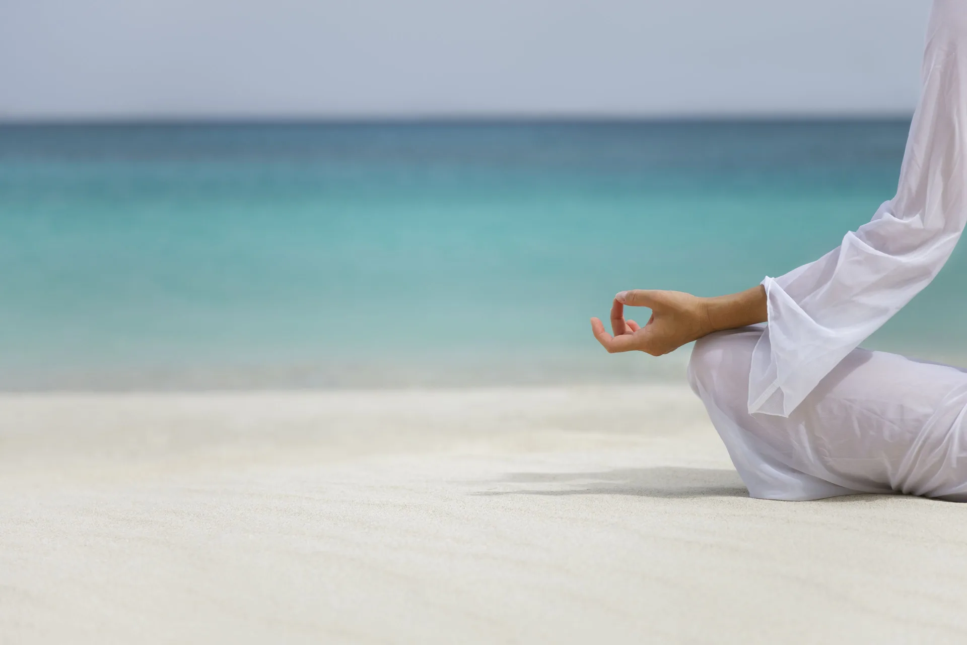 A person meditates on the white sand beside turquoise water at Sandyport Beach Resort.