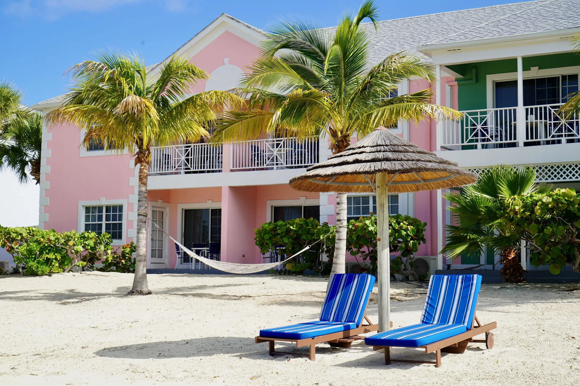 Beachfront pastel building, palms, loungers and a hammock at Sandyport Beach Resort.