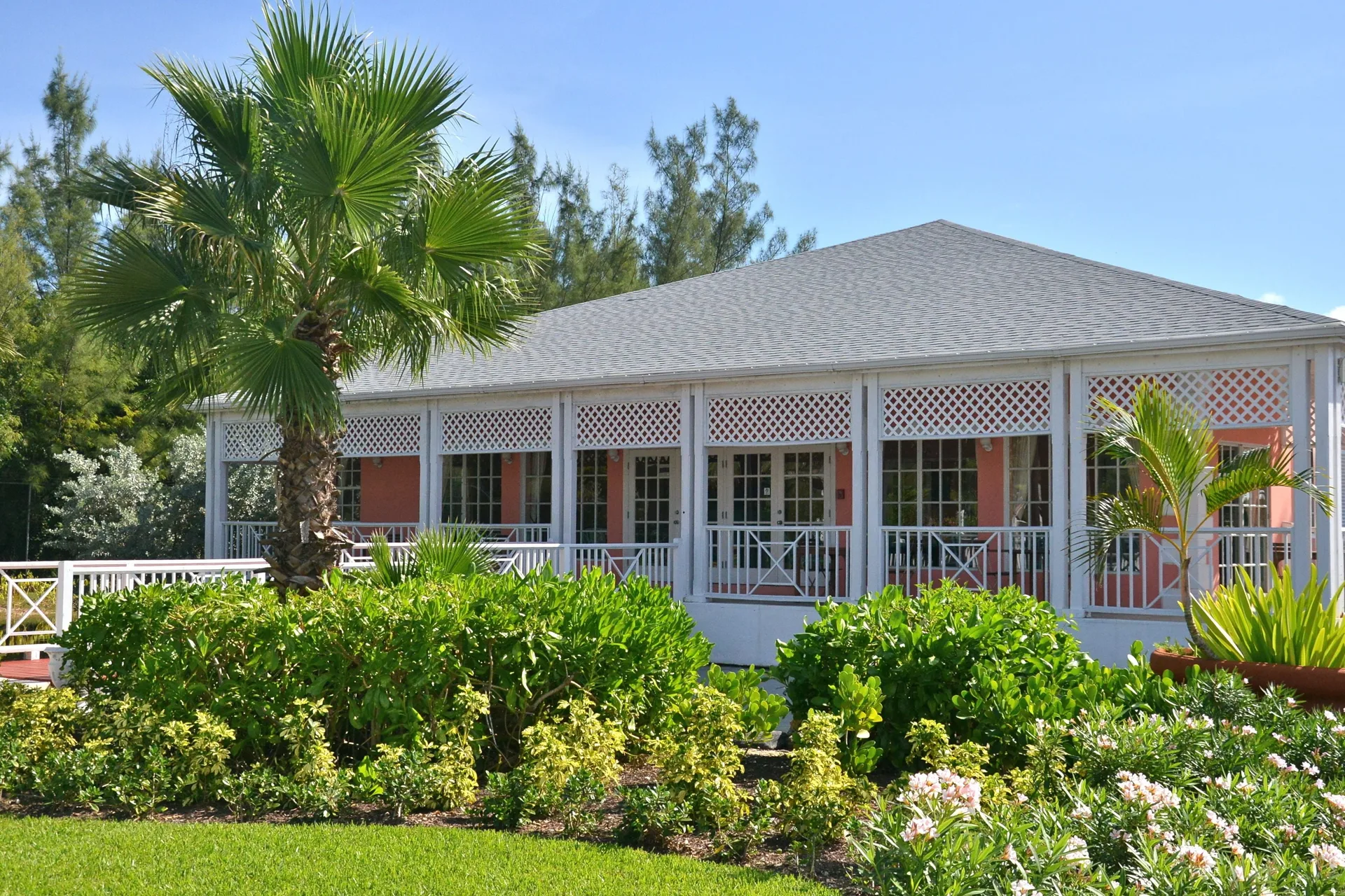 A pink building with a wraparound porch sits among tropical gardens at Sandyport Beach Resort.