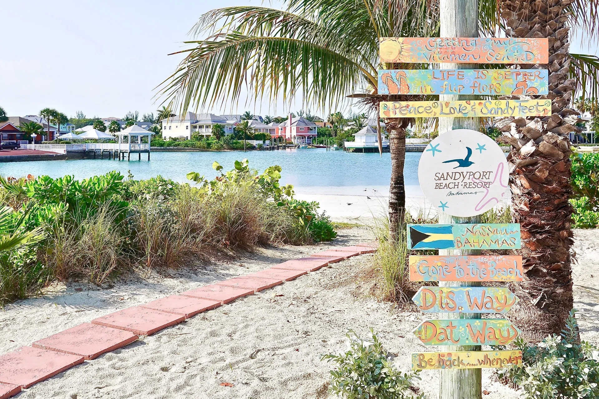 Colorful Sandyport Beach Resort sign beside a sandy lagoon path.