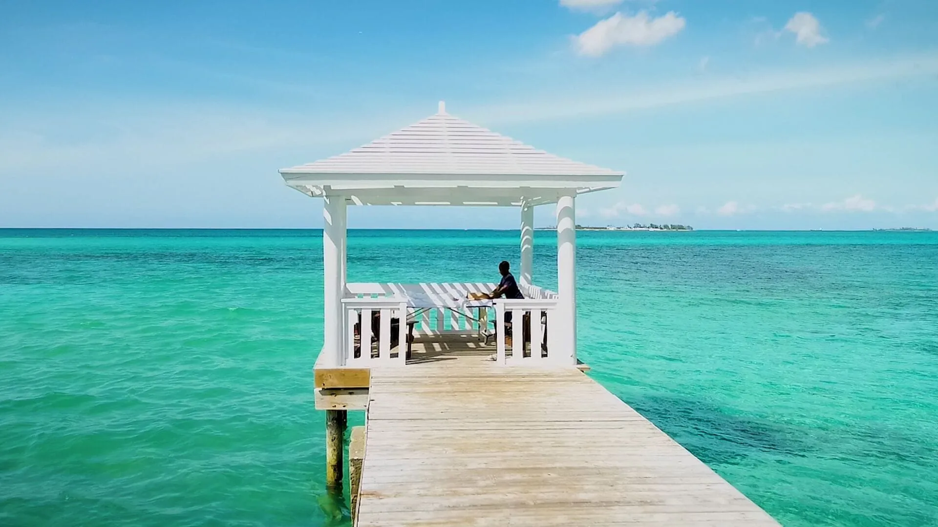 A white gazebo at the end of a wooden pier overlooks turquoise water at Sandyport Beach Resort.