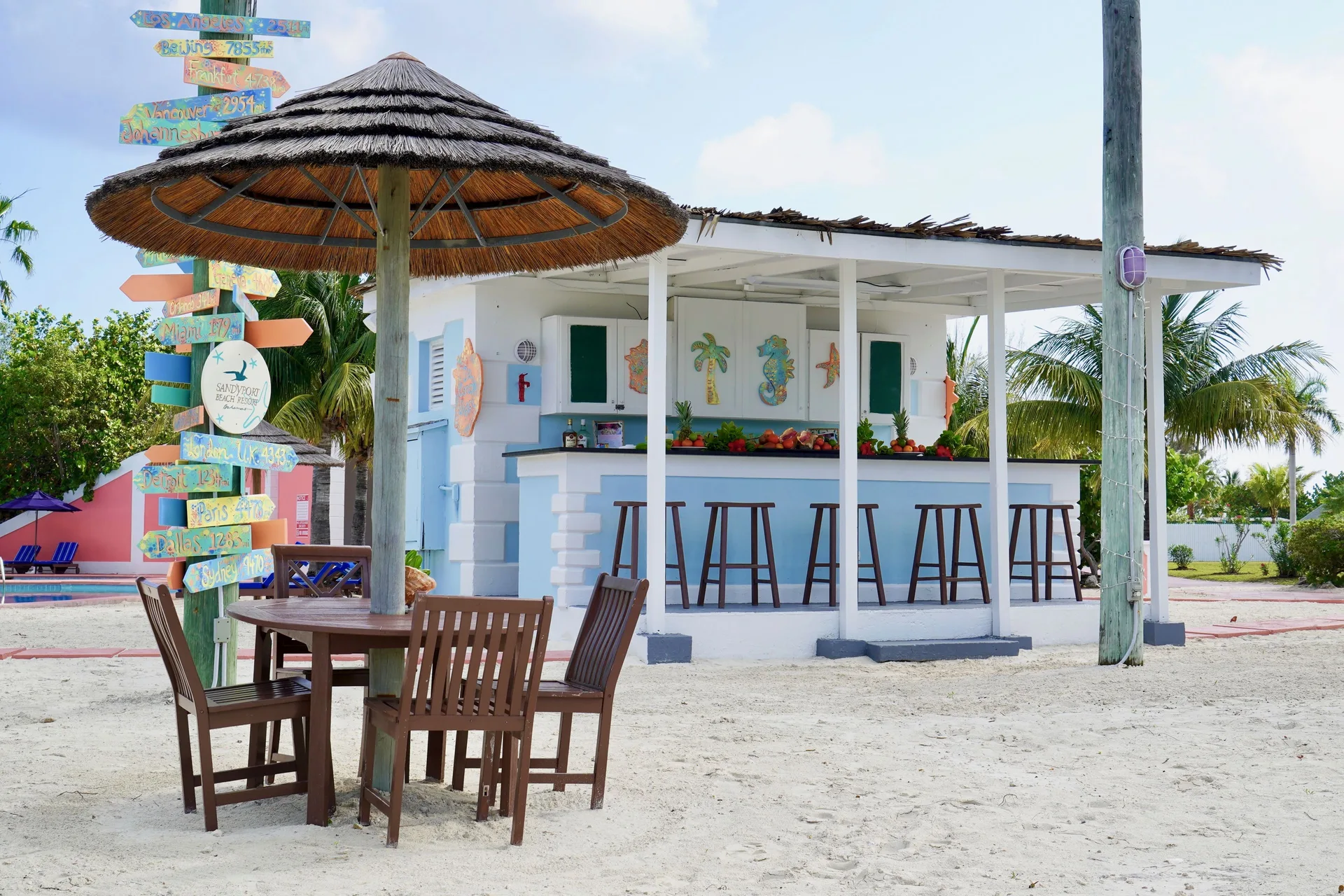 Sandy outdoor bar with stools and thatched seating at Sandyport Beach Resort.