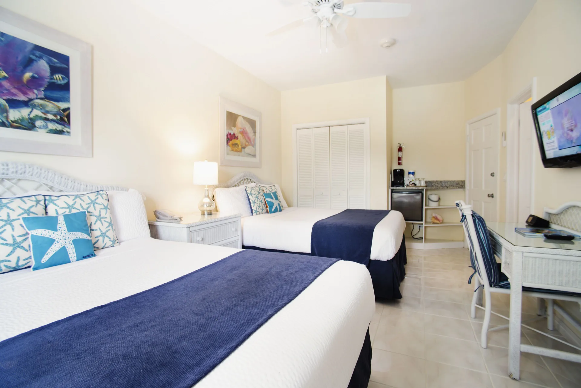 Standard Room with two beds, TV, desk, closet, and refreshment area at Sandyport Beach Resort.