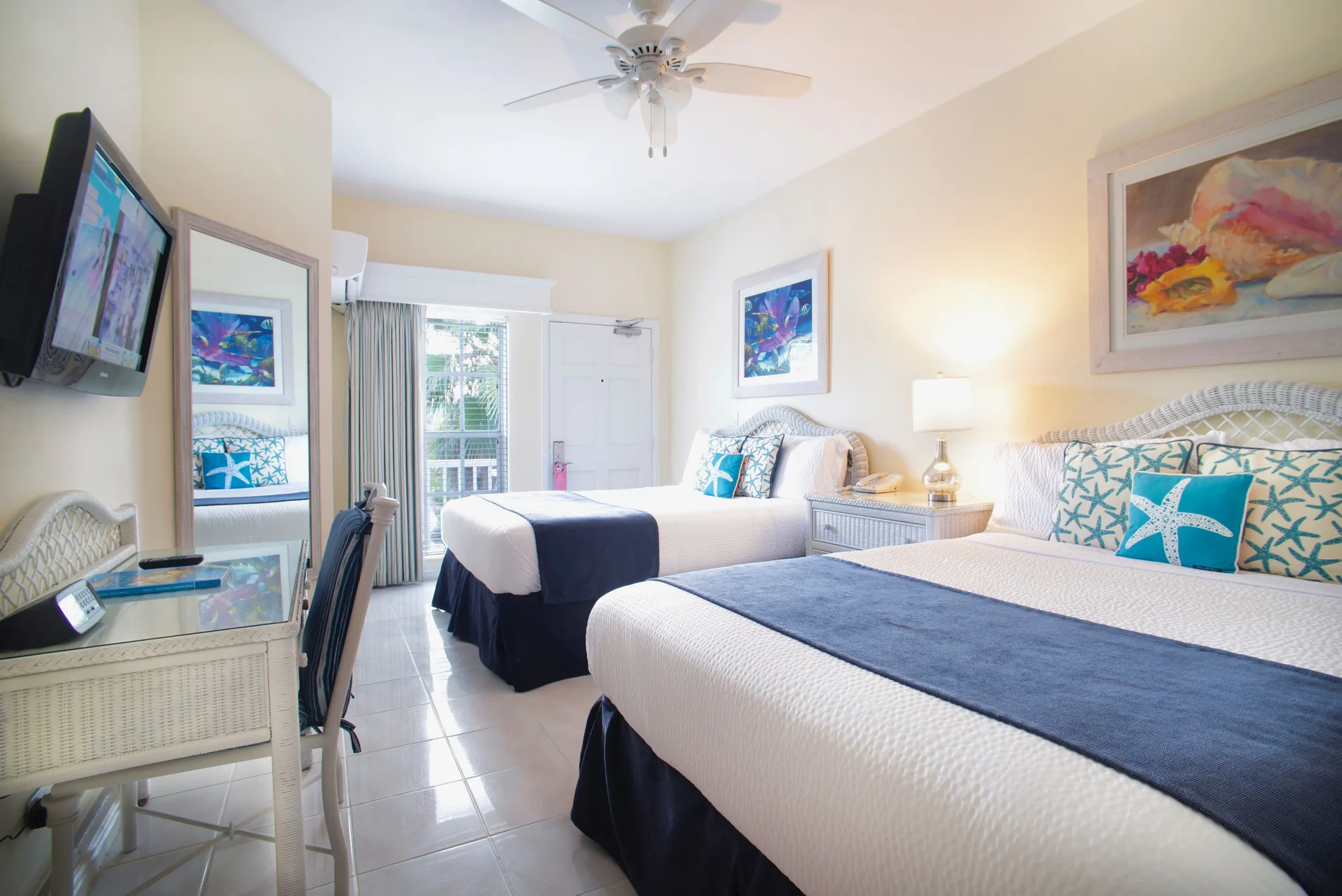 Standard Room with two beds, desk, mirror, and balcony door at Sandyport Beach Resort.
