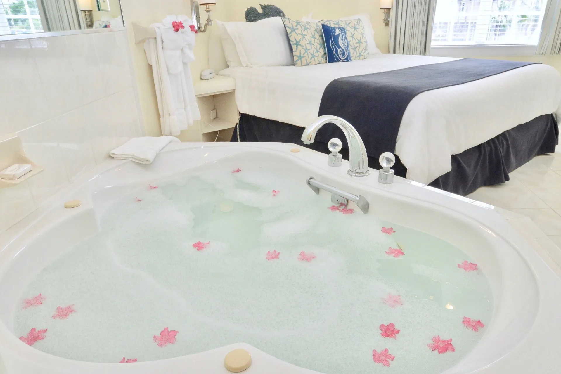 Jetted tub with pink petals beside a white bed in a suite at Sandyport Beach Resort.