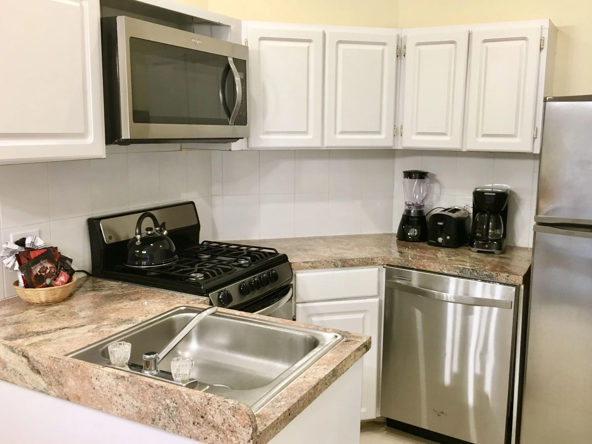 Compact suite kitchen with stove, sink, dishwasher, and small appliances at Sandyport Beach Resort.
