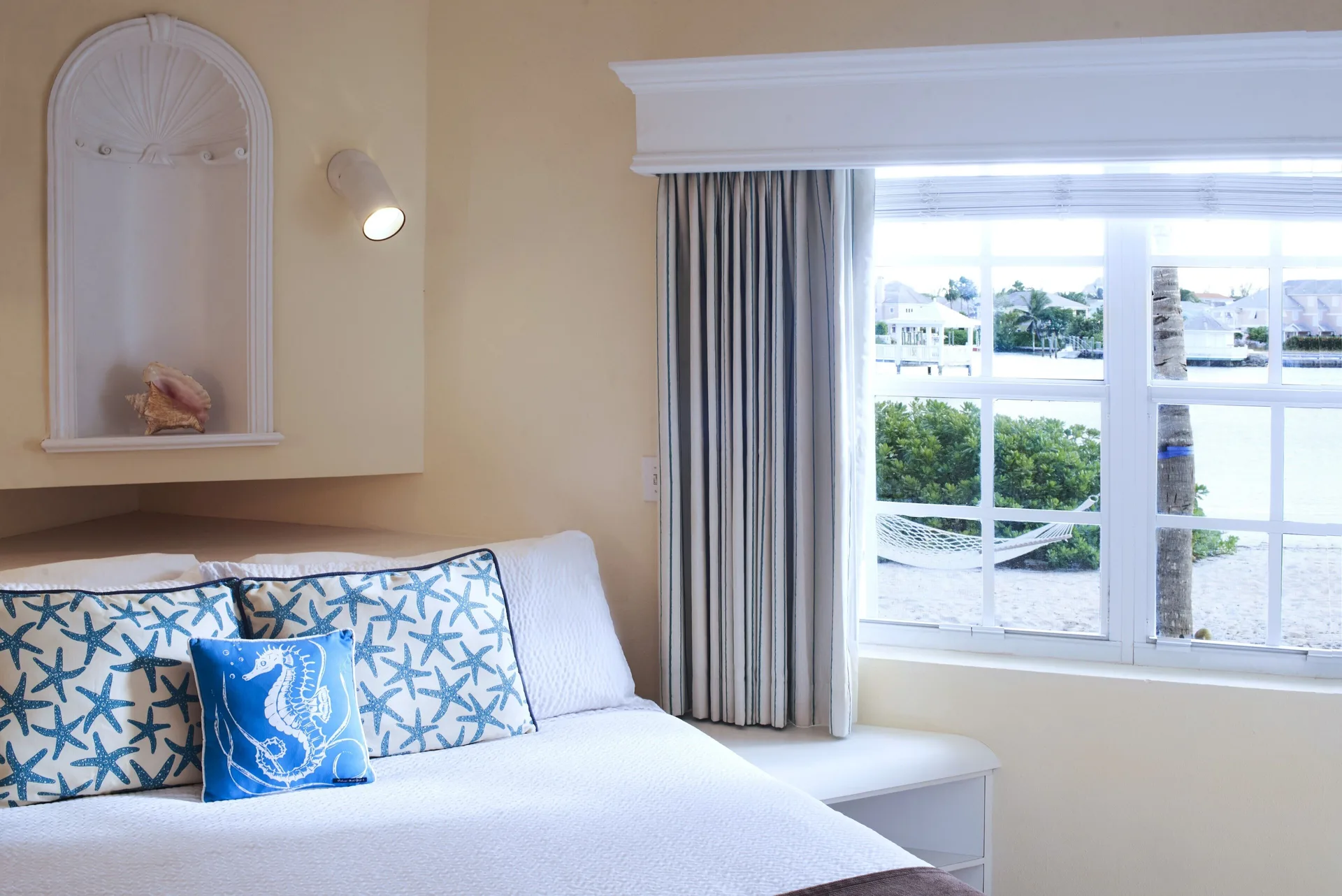 White bed with starfish pillows beside a window and lagoon view at Sandyport Beach Resort.