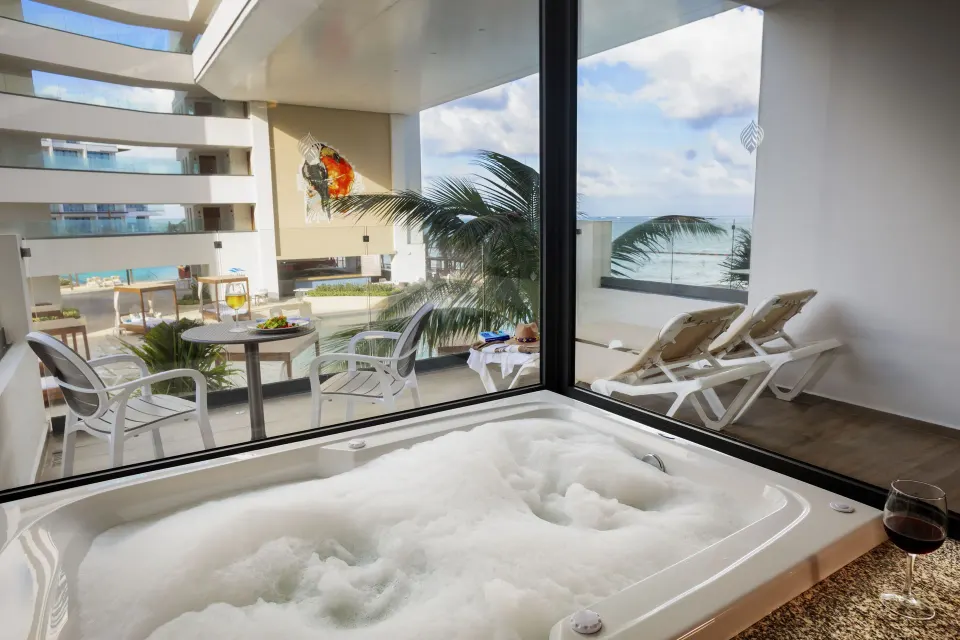 Amber Room soaking tub beside glass doors and ocean-view balcony at Sensira Resort & Spa Riviera Maya.