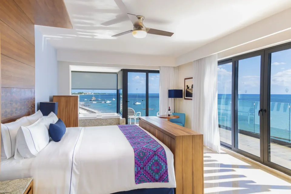 Ruby Suite king bed with balcony doors and blue ocean views at Sensira Resort & Spa Riviera Maya.