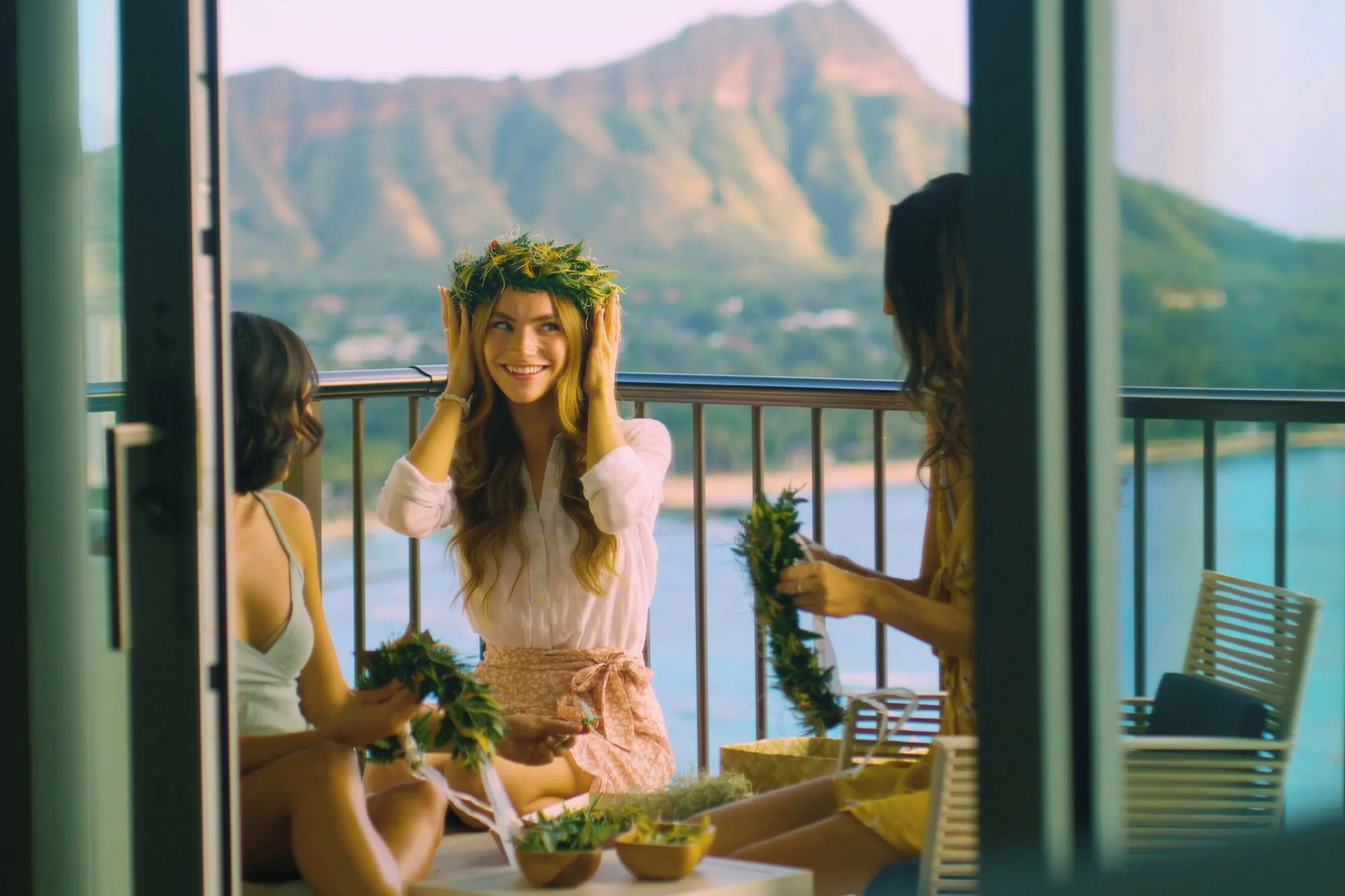 Guests make flower leis on a balcony at Sheraton Waikiki Beach Resort with Diamond Head in the background.