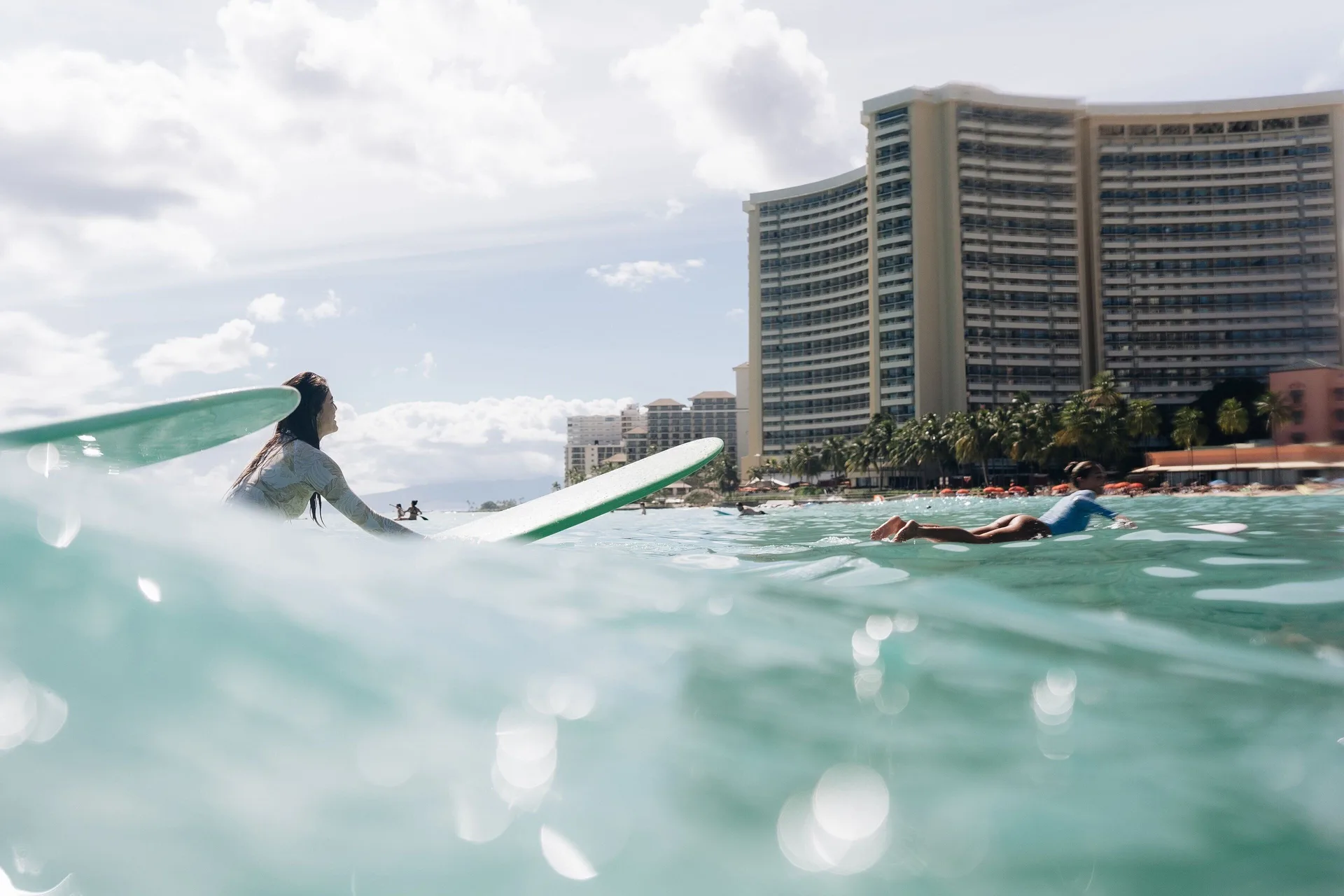 Surfers floating offshore with the resort tower behind Sheraton Waikiki Beach Resort.