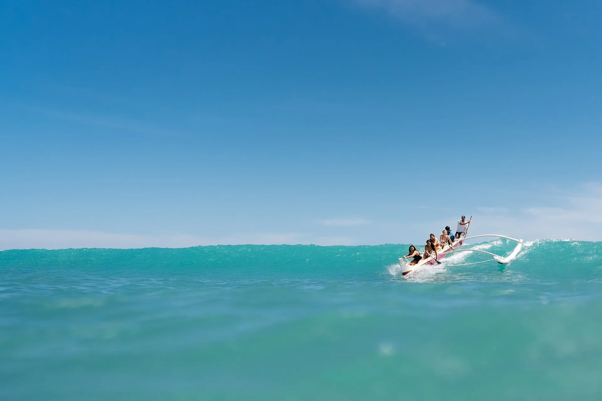 Outrigger canoe riding a turquoise wave off Sheraton Waikiki Beach Resort.