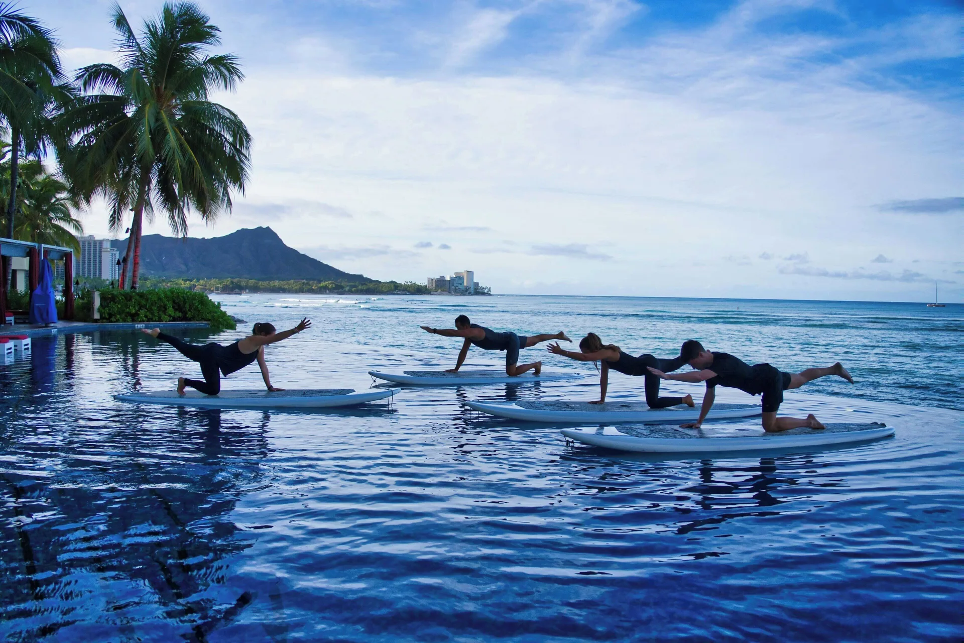 Guests practice paddleboard yoga in the pool at Sheraton Waikiki Beach Resort.