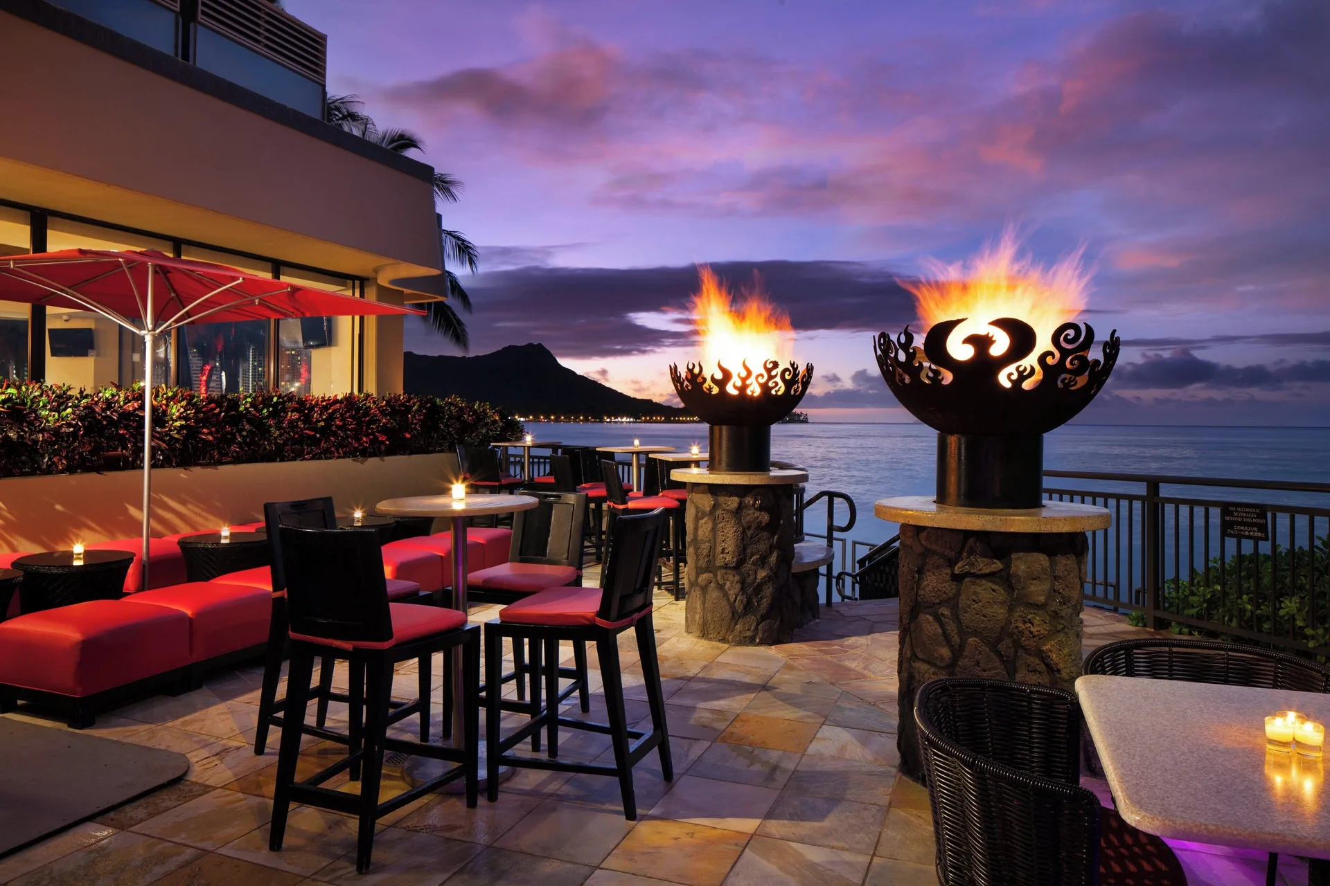 Oceanfront terrace with fire bowls at Sheraton Waikiki Beach Resort at sunset.