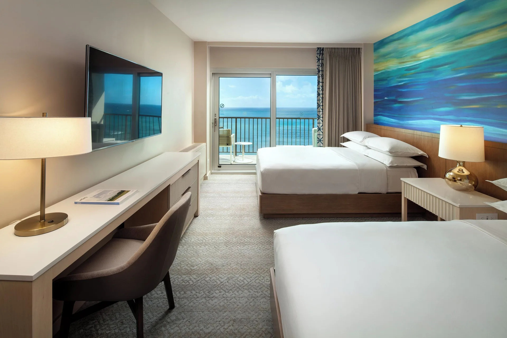 Oceanfront guest room with two beds and balcony view at Sheraton Waikiki Beach Resort.