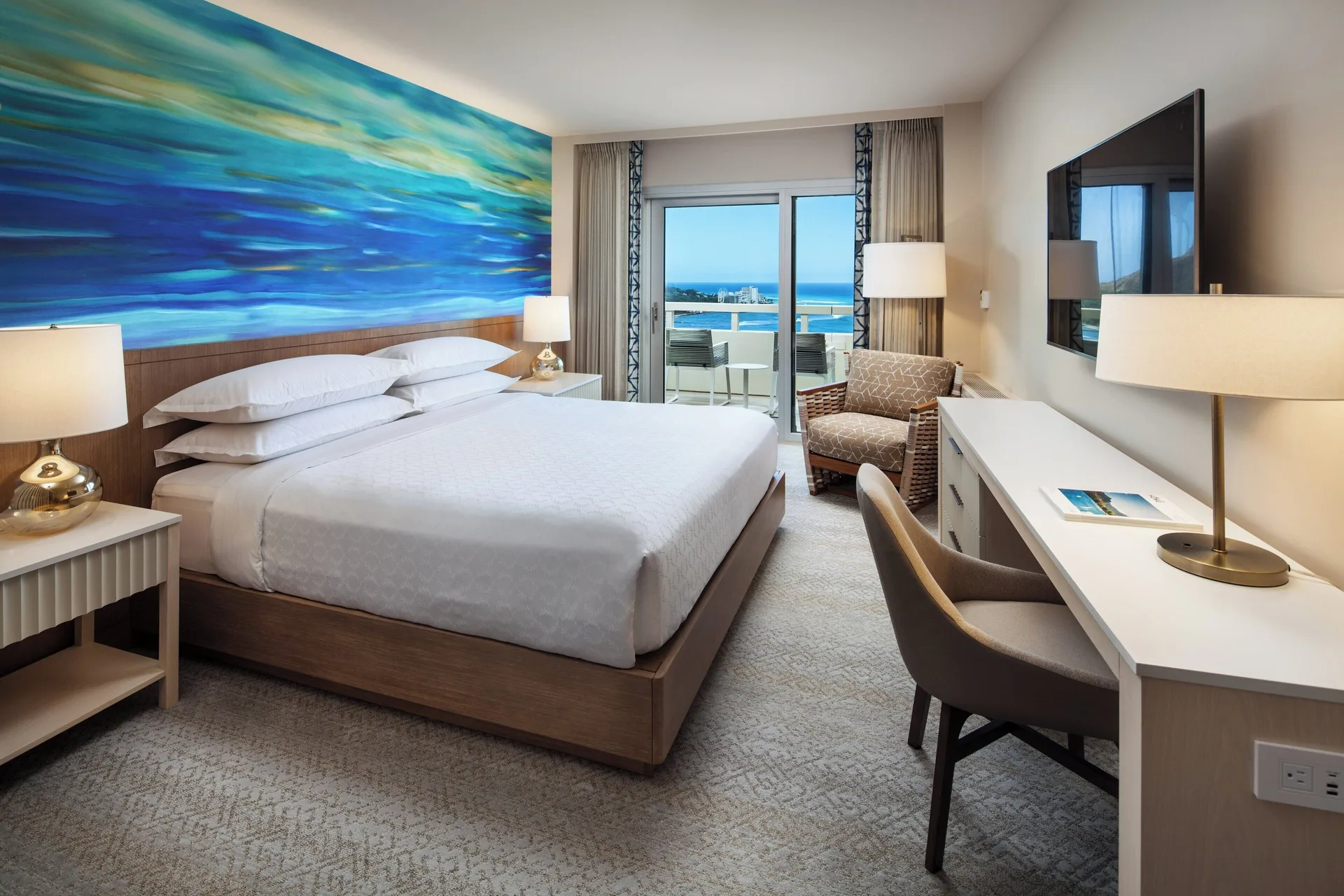 Oceanfront king guest room with desk, TV, and balcony at Sheraton Waikiki Beach Resort.