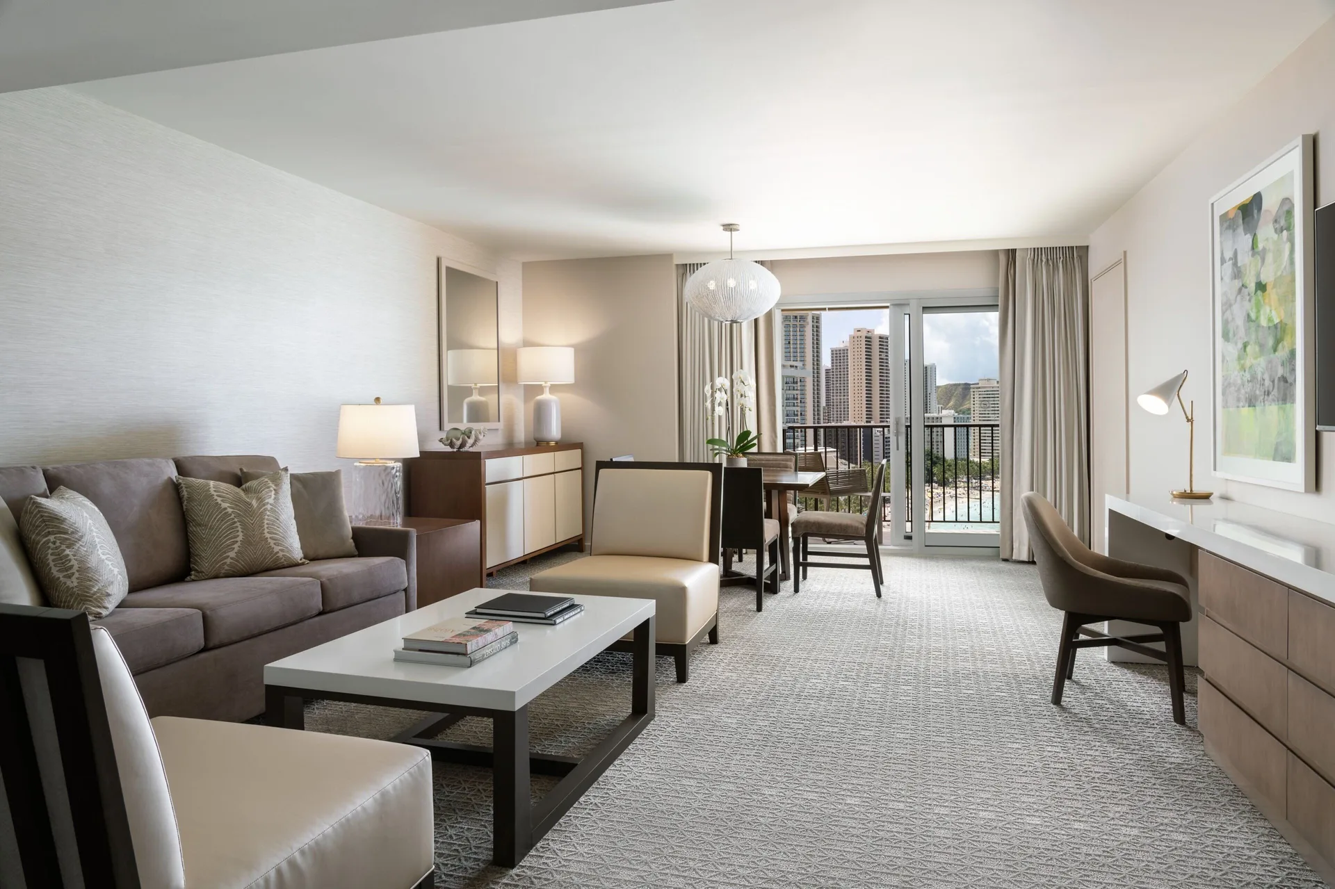 Malia Suite living room with sofa, desk, dining table and balcony at Sheraton Waikiki Beach Resort.