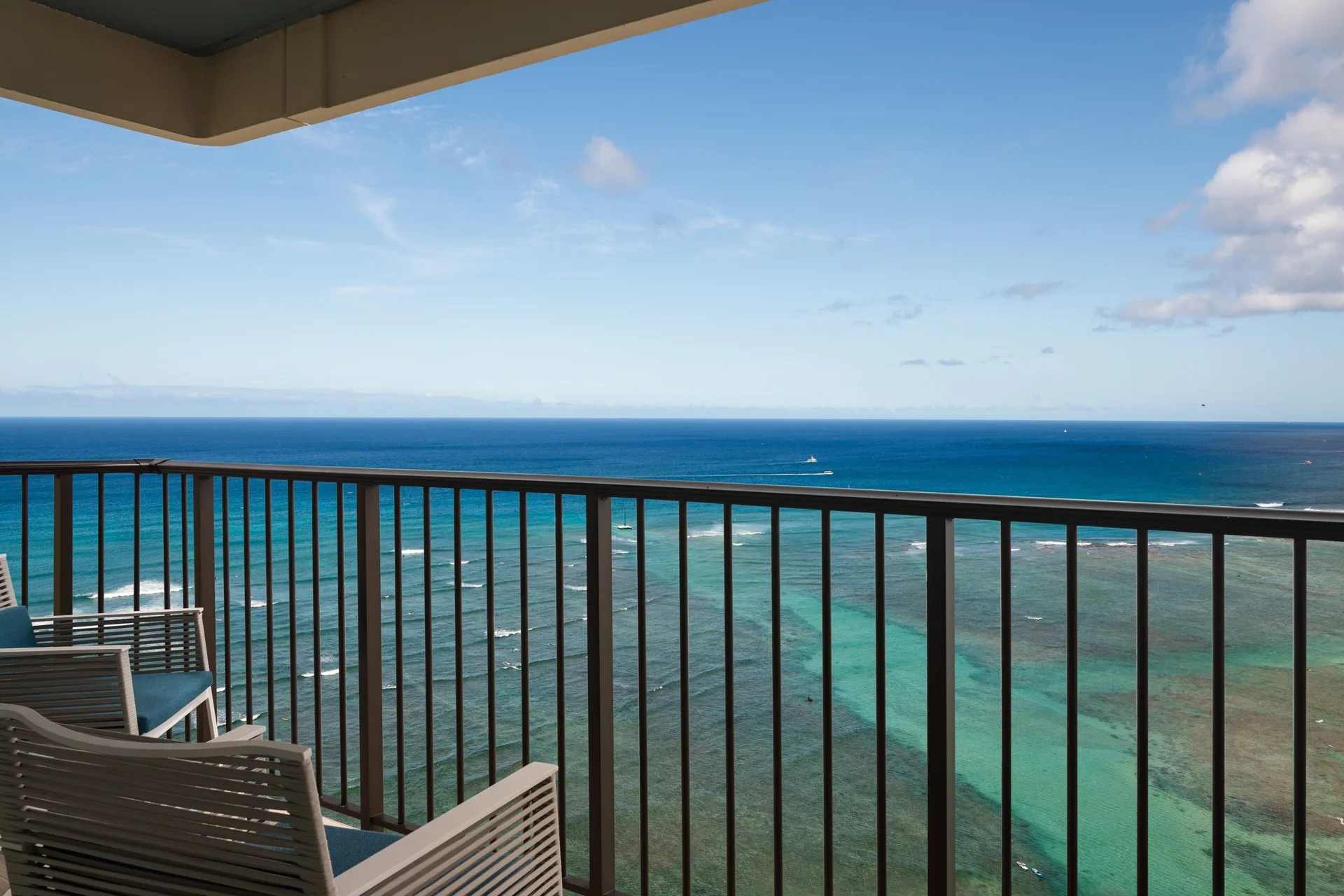 Oceanfront suite balcony with chairs and Pacific view at Sheraton Waikiki Beach Resort.