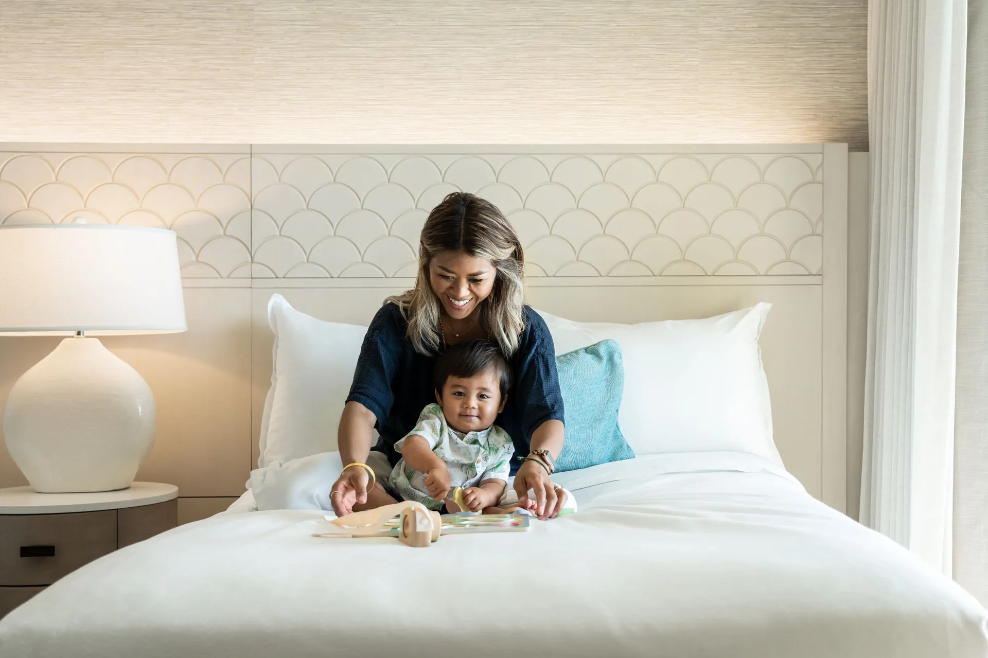 Ohana Suite bed at Sheraton Waikiki Beach Resort with a family reading on the white bedding.