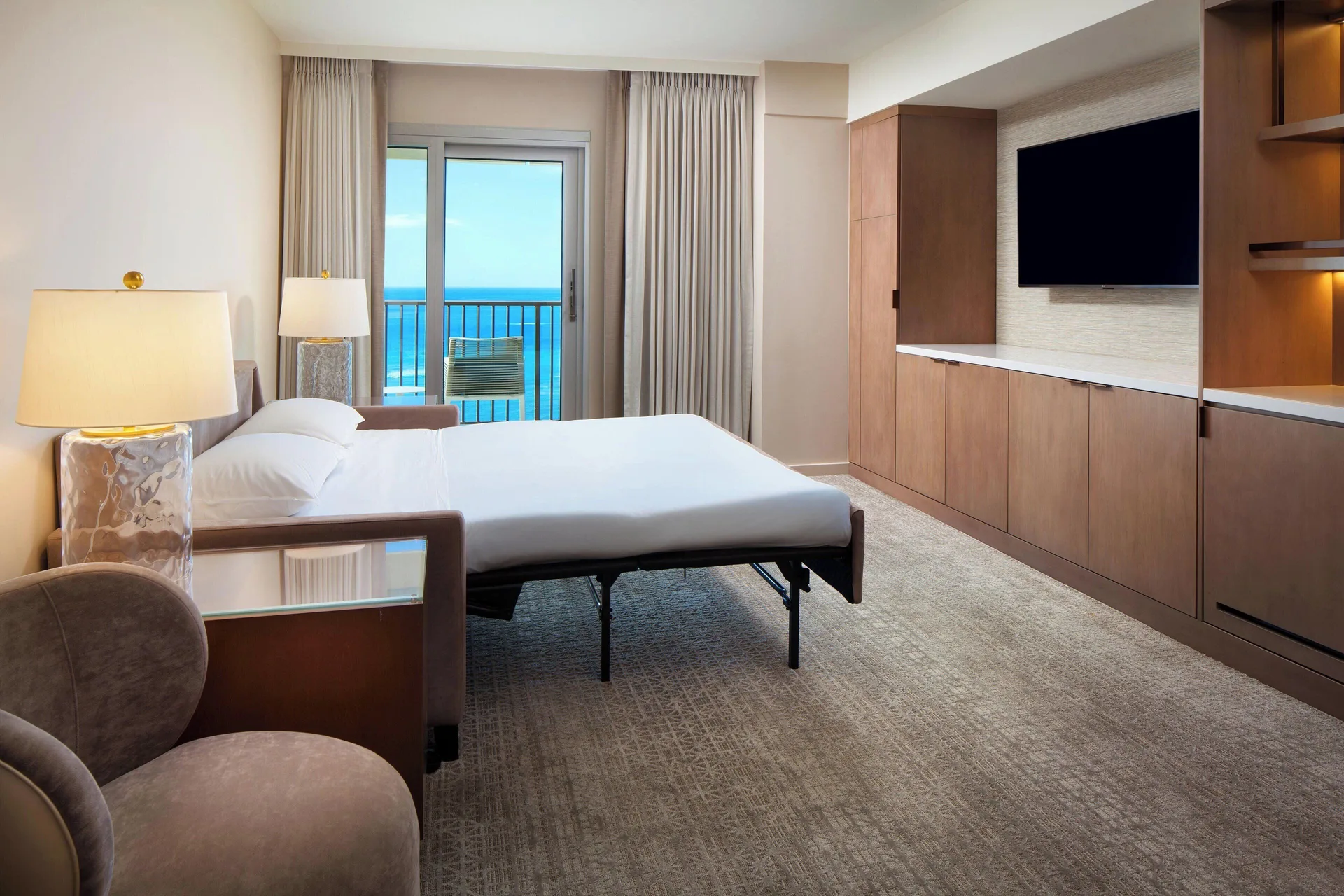 Oceanfront Ohana Suite bedroom at Sheraton Waikiki Beach Resort with sofa bed and wall-mounted TV.