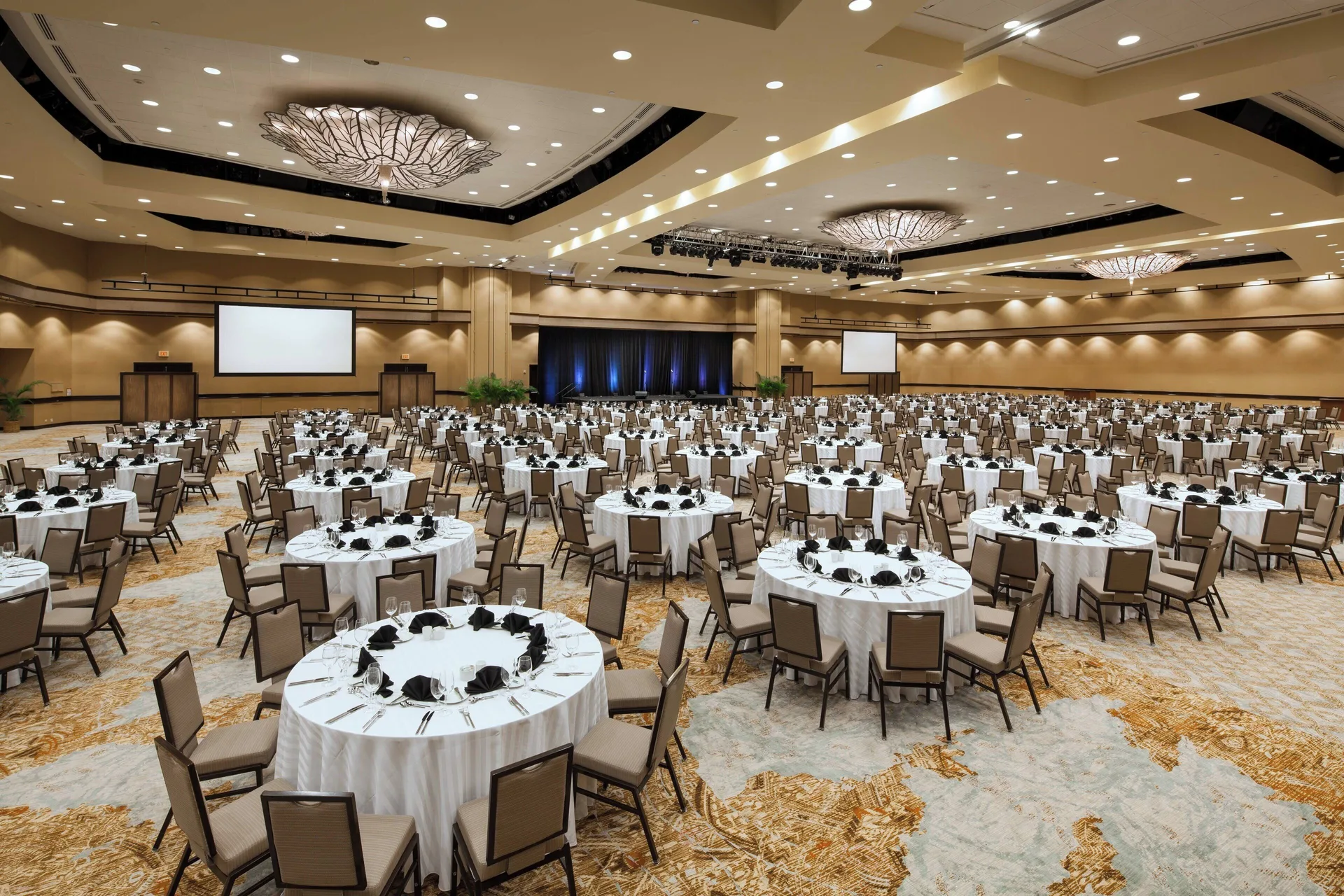 Grand ballroom set for a banquet with stage and screens at Sheraton Waikiki Beach Resort.