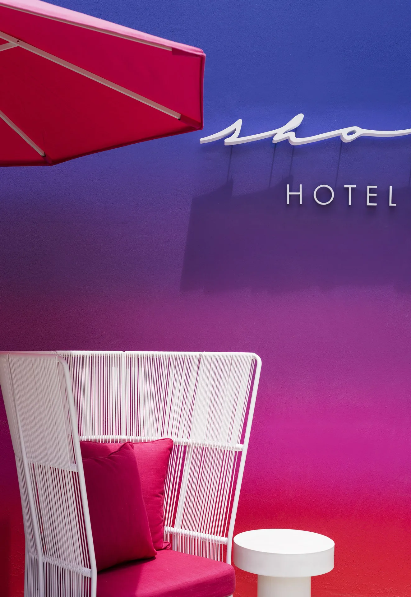 White patio chair, pink umbrella, and hotel sign wall at Shoreline Hotel Waikiki.