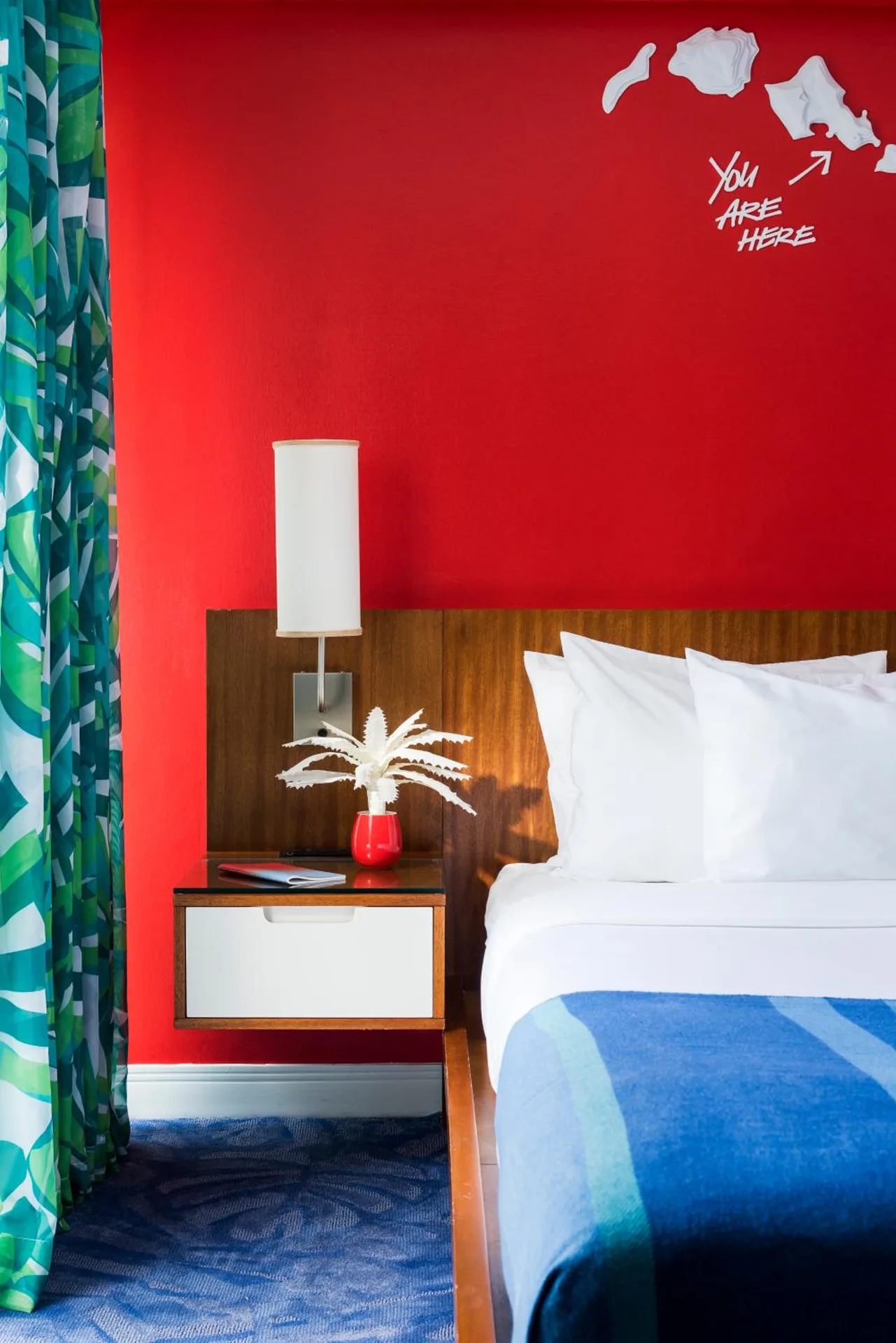 Guest room bed with red wall, white pillows, and map art at Shoreline Hotel Waikiki.