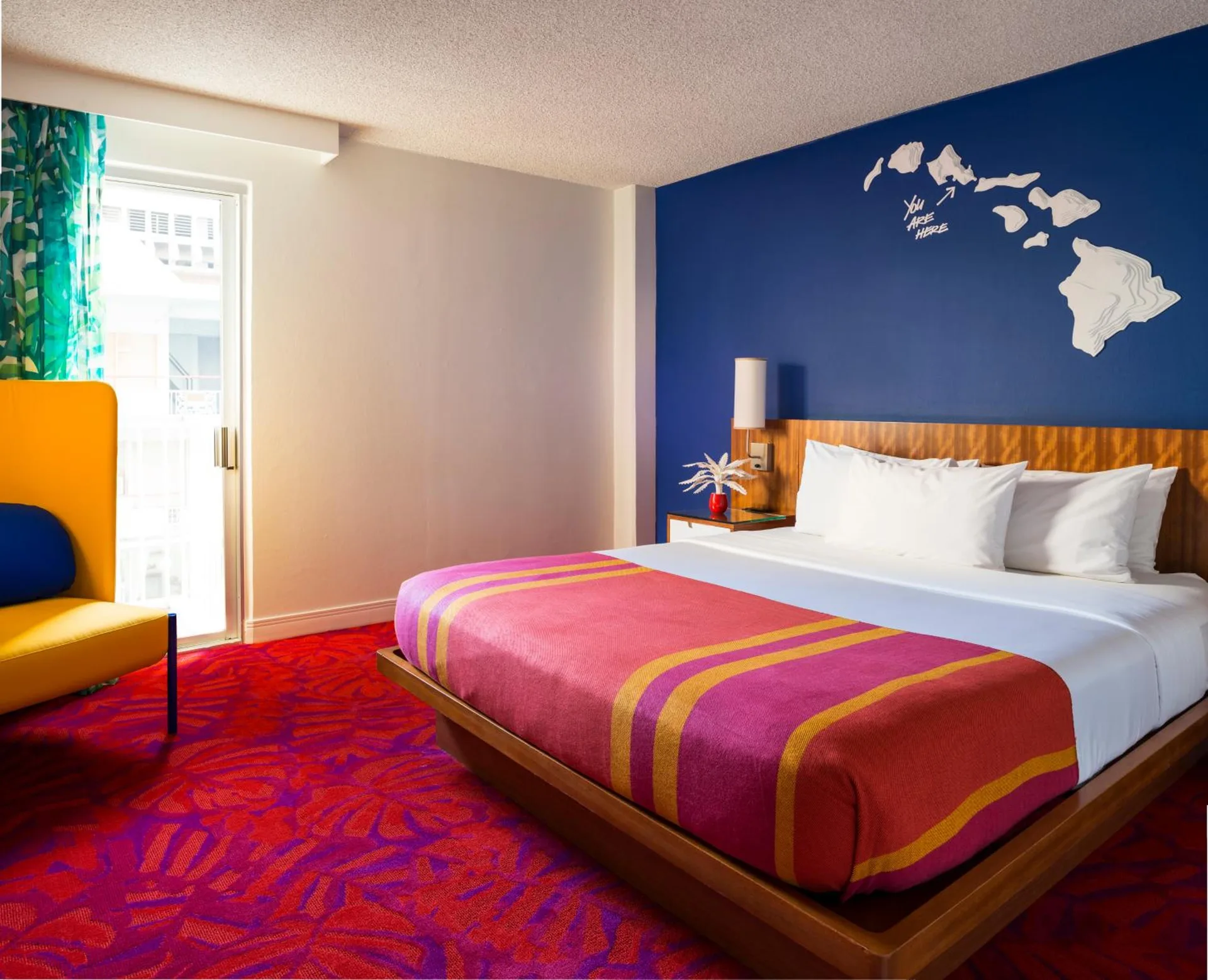 Guest room with king bed, blue wall, and yellow chair at Shoreline Hotel Waikiki.