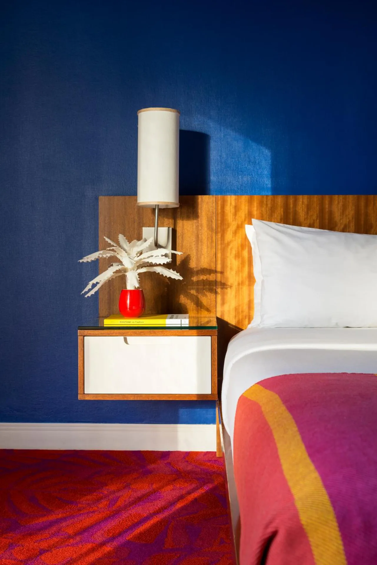 Guest room bed and floating nightstand with blue wall at Shoreline Hotel Waikiki.