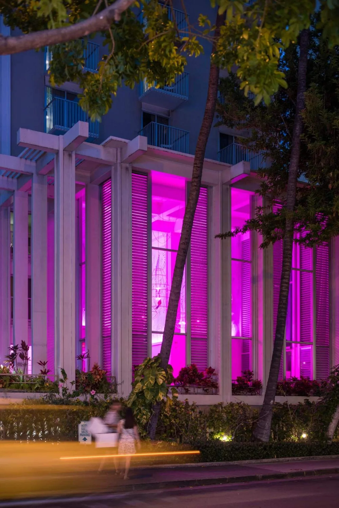 Neon-lit exterior of Shoreline Hotel Waikiki with palms and balconies at night.