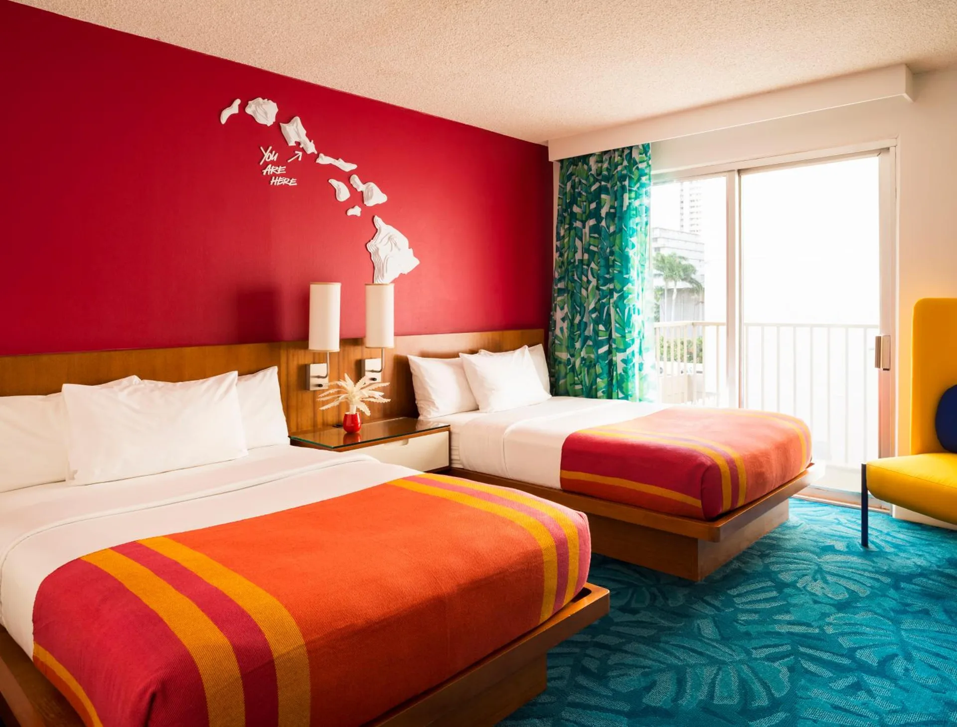 Colorful two-bed guest room with balcony doors at Shoreline Hotel Waikiki.