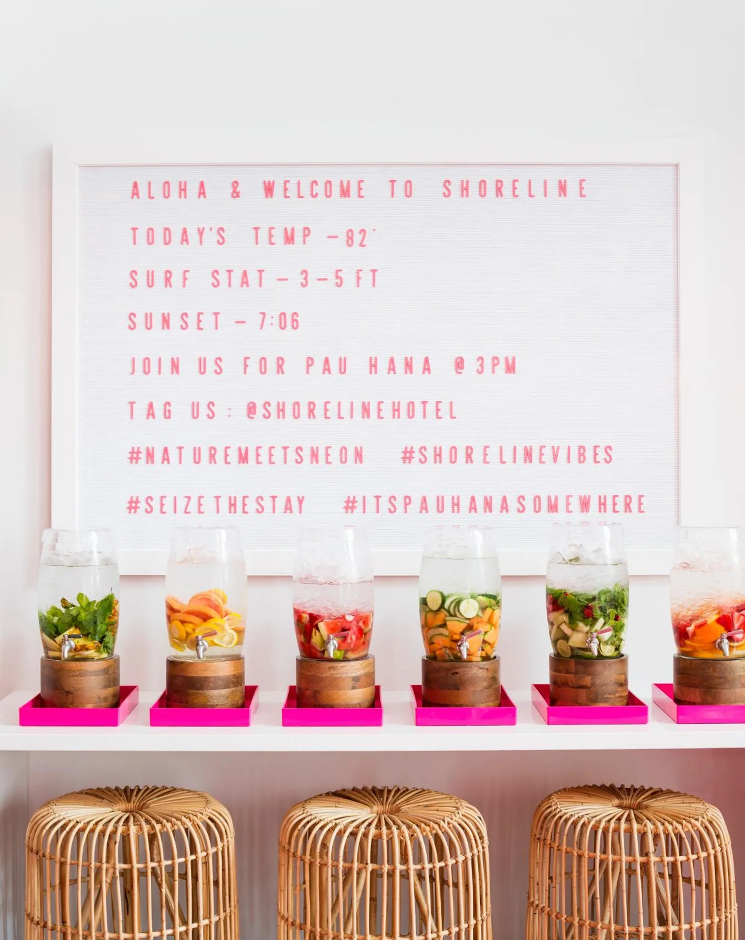 Welcome sign, fruit-infused drink dispensers, and rattan stools at Shoreline Hotel Waikiki.