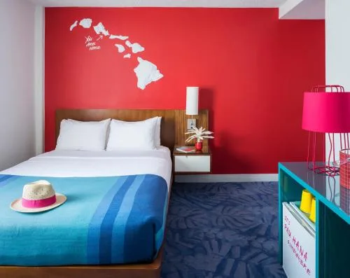 One-bed guest room with red wall and blue bed runner at Shoreline Hotel Waikiki.