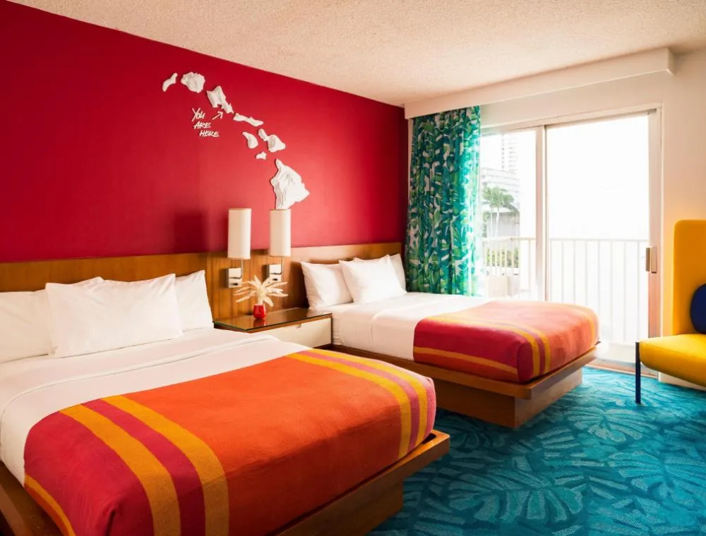 Two-bed guest room with red wall and balcony doors at Shoreline Hotel Waikiki.