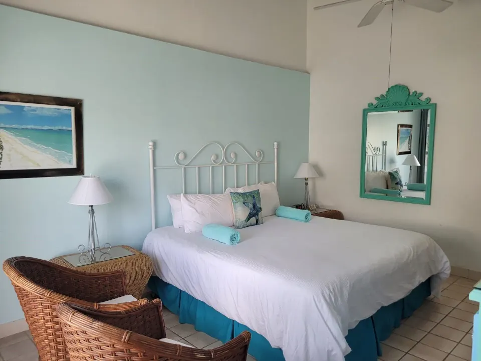 Balcony Room king bed with wicker chair, lamps and turquoise mirror at Sibonné Beach Hotel.