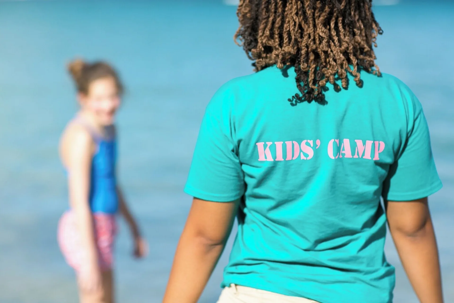Kids' camp staff member by the water with a child at The Buccaneer Beach & Golf Resort.