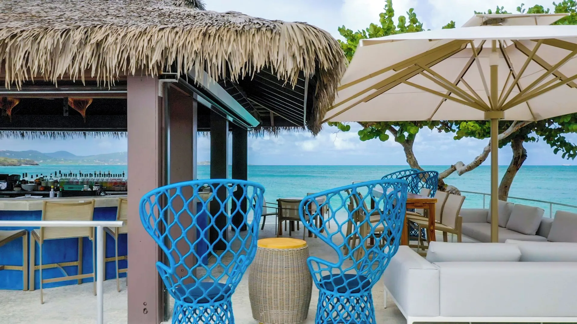 Beach bar seating and blue chairs face the ocean at The Buccaneer Beach & Golf Resort.