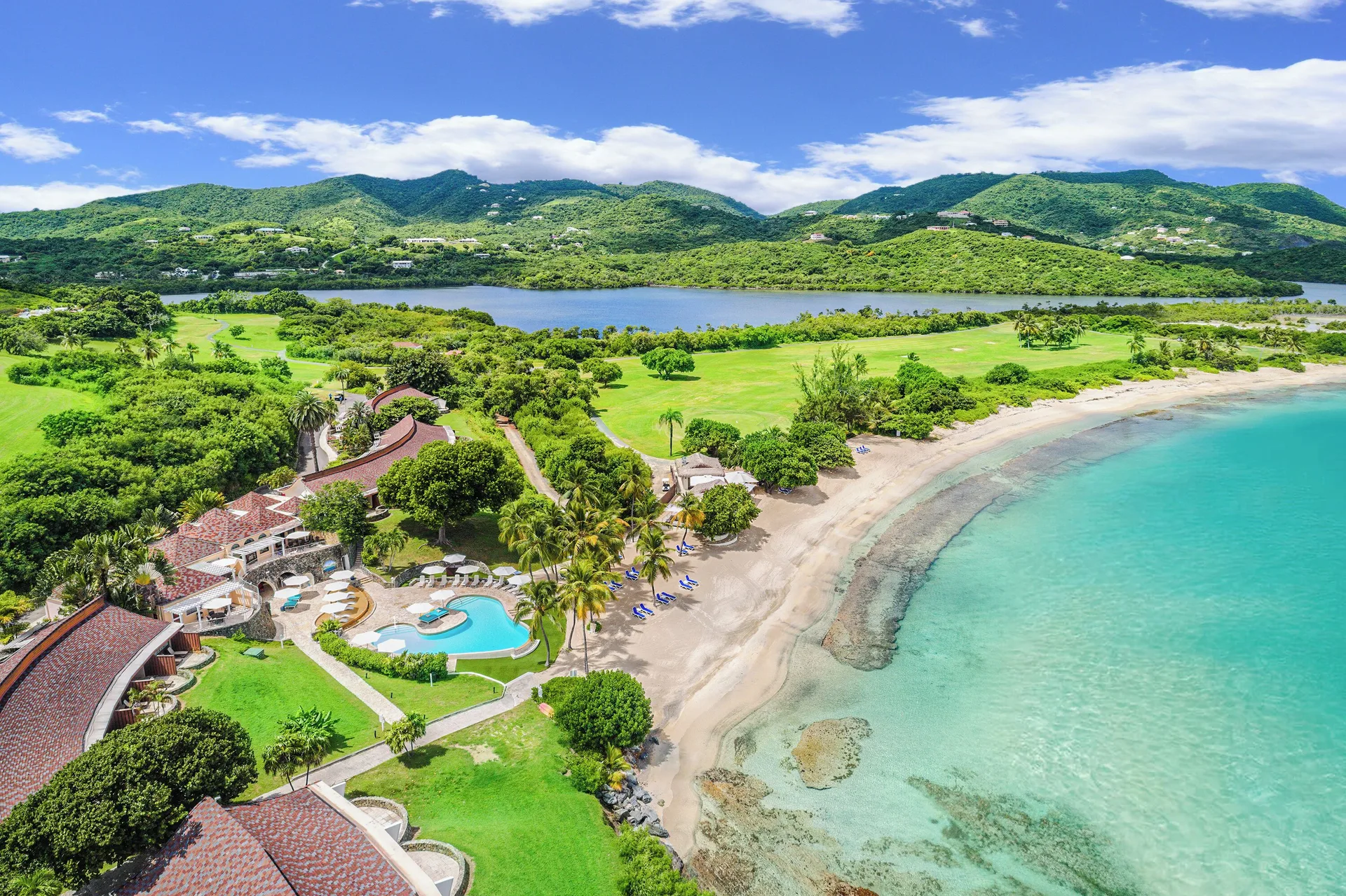 Aerial view of The Buccaneer Beach & Golf Resort coastline, beach, pool, golf greens, and hills