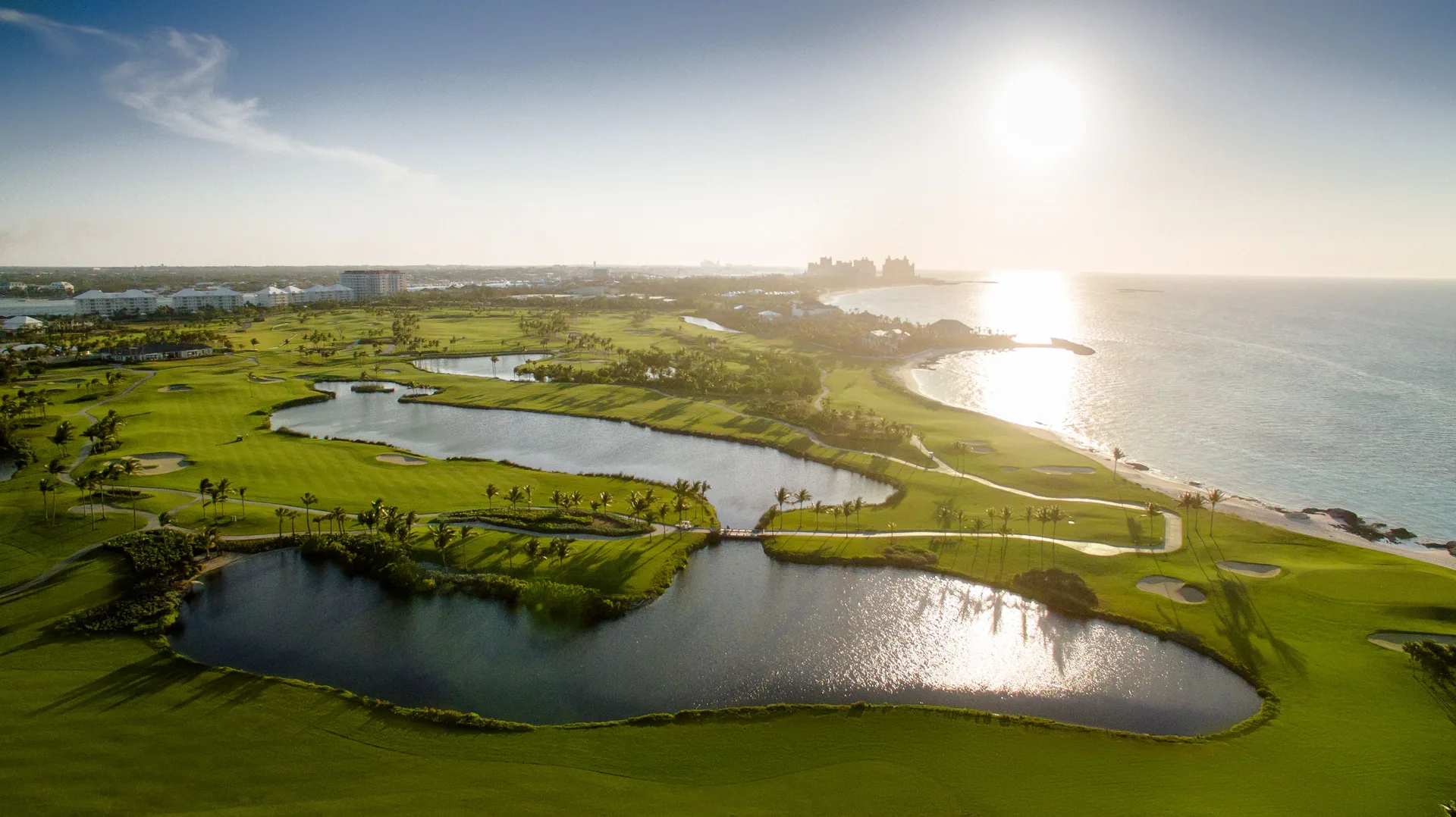 Aerial sunset view of golf greens, ponds, and coastline at The Coral at Atlantis.