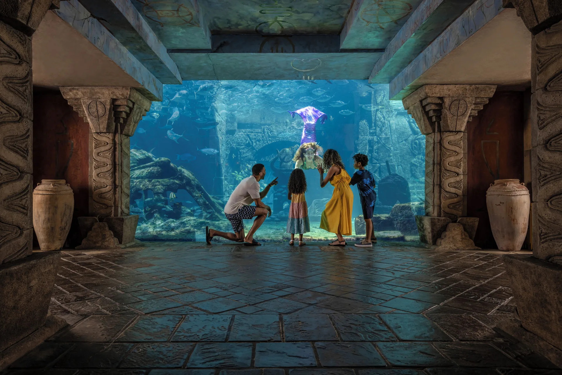 A family watches a mermaid performer in an aquarium window at The Coral at Atlantis.