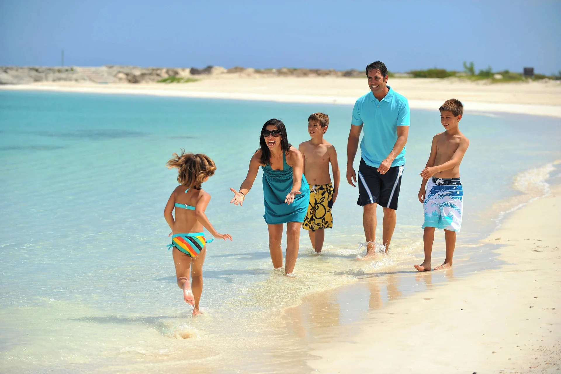 A family walks through shallow turquoise water at The Coral at Atlantis.