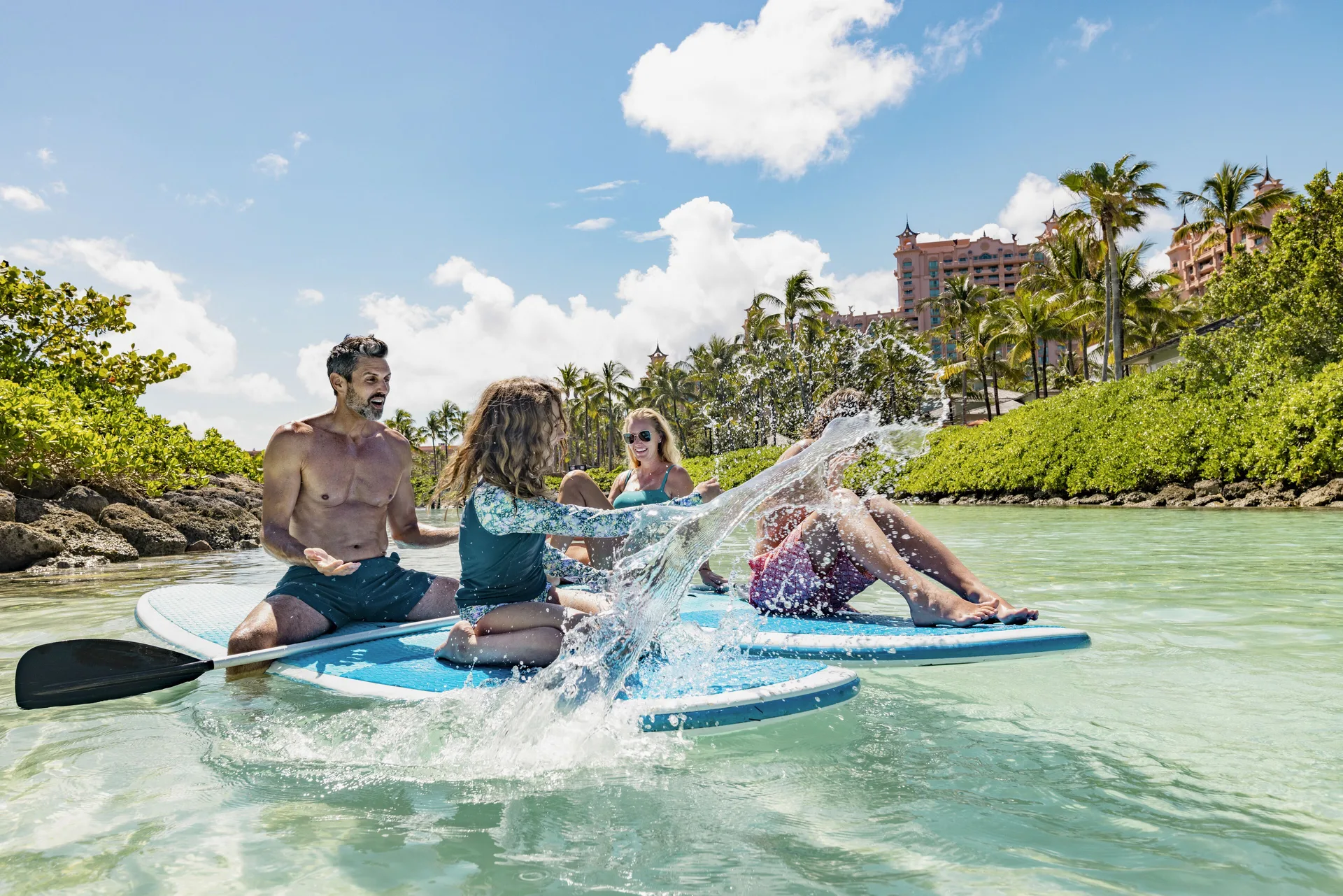 Guests paddleboard in shallow turquoise water near palms at The Coral at Atlantis.