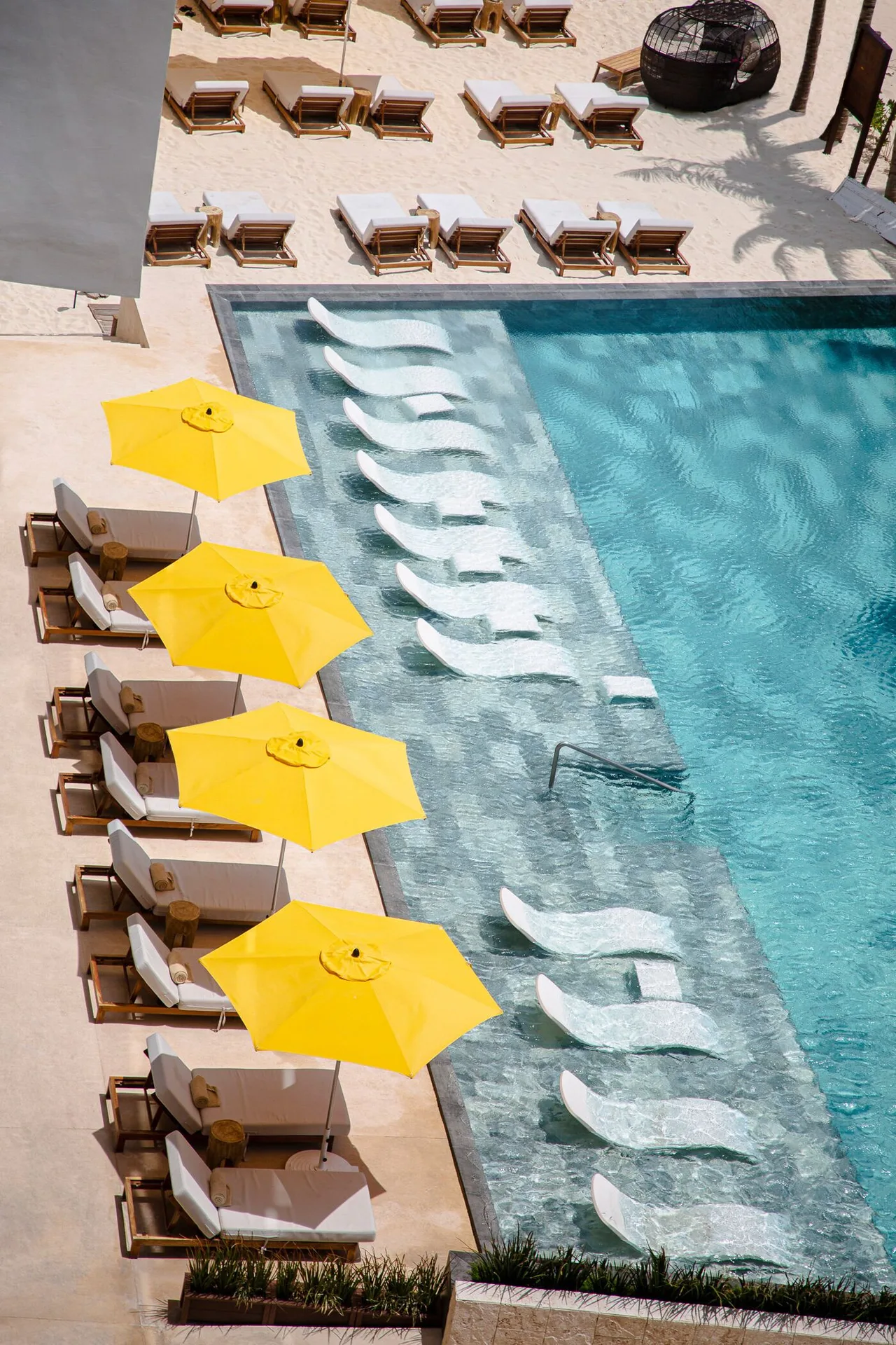 Pool deck with yellow umbrellas, sunbeds, and in-water loungers at The Fives Oceanfront Riviera Maya.